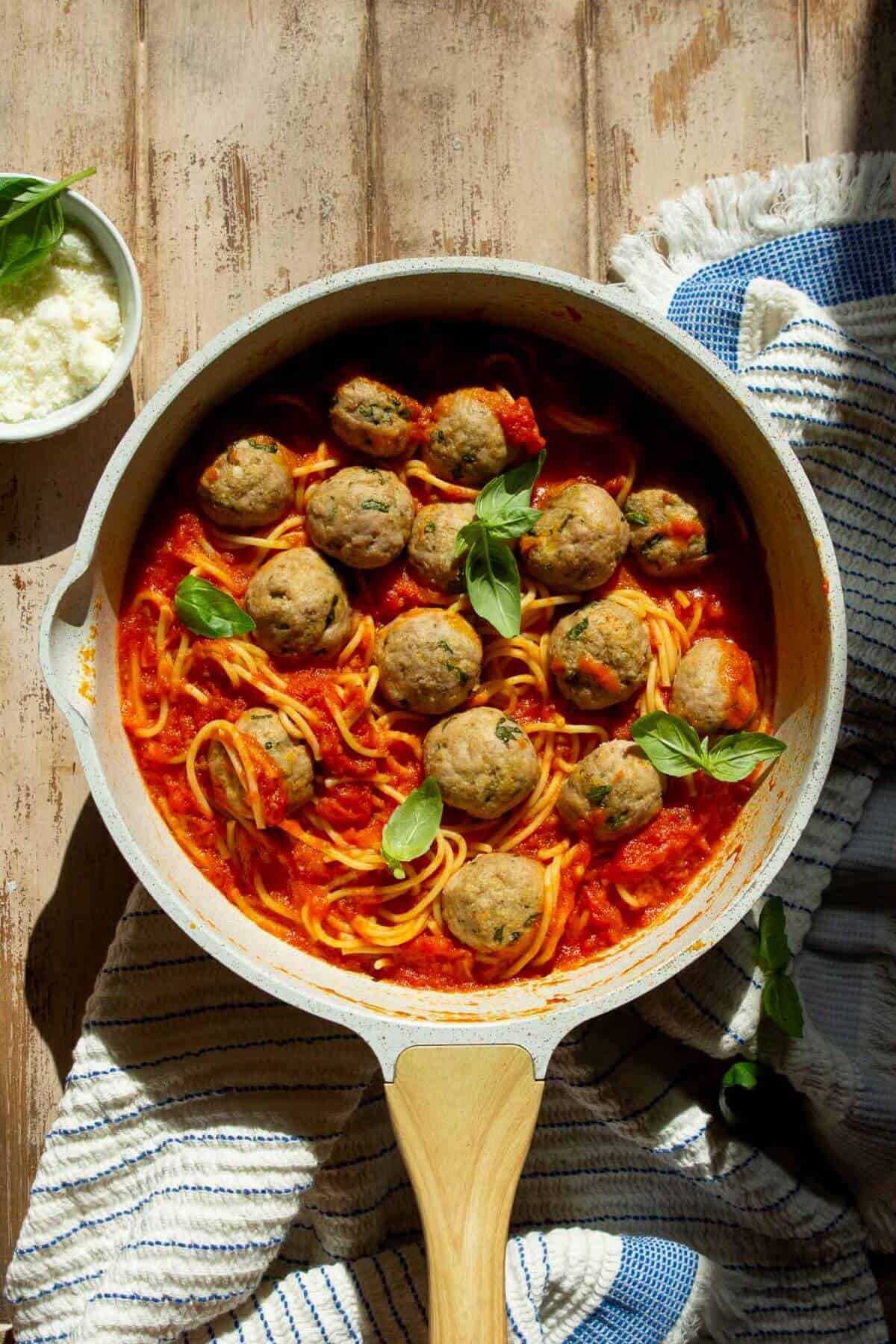 Easy and juicy air fryer turkey meatballs in a pan with red sauce, pasta, and fresh basil.