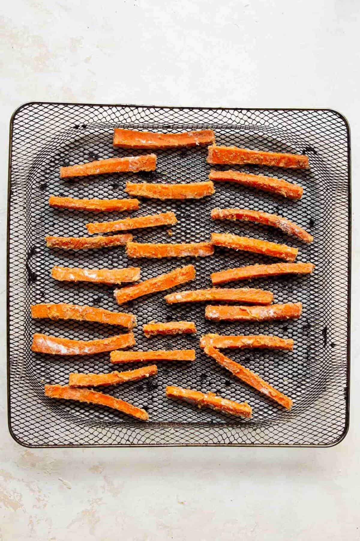 Seasoned carrot stick in air fryer basket before cooking.