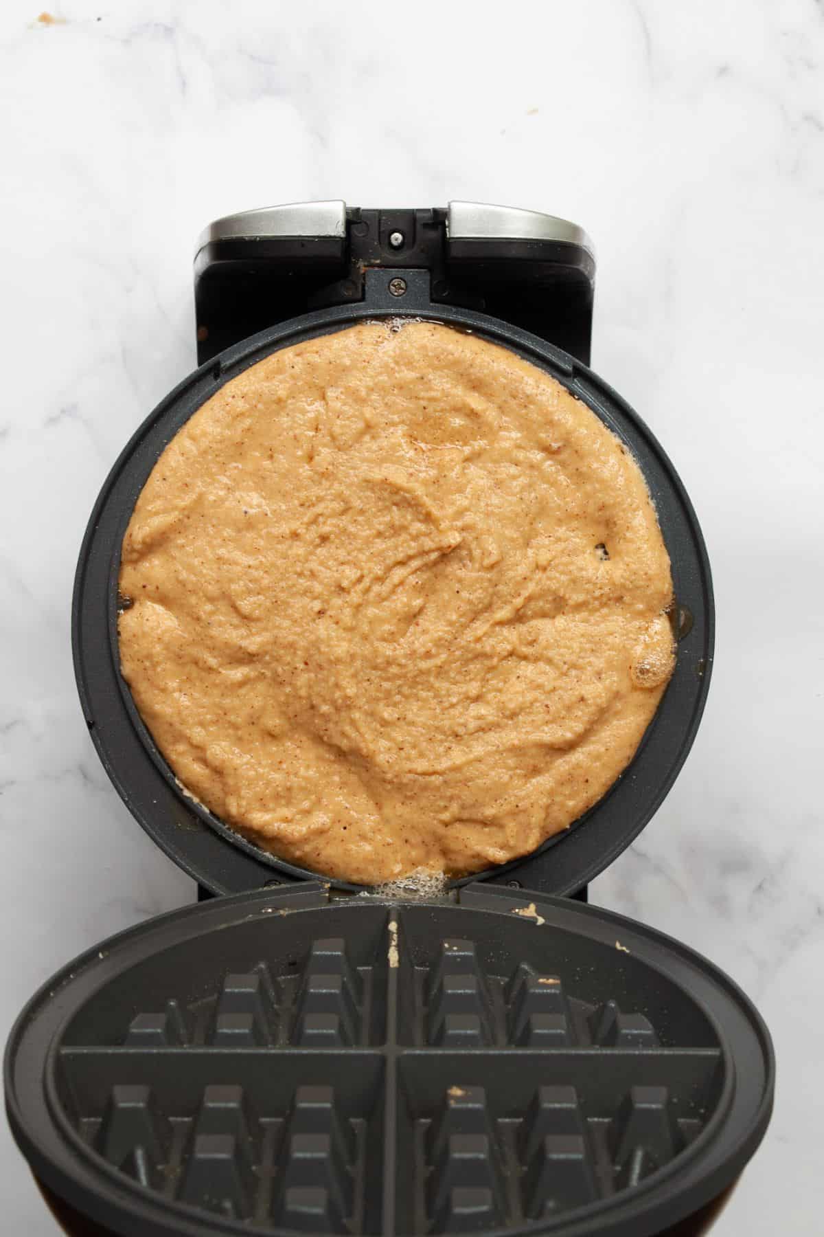 Almond flour waffle batter poured into a preheated round waffle iron, ready to cook.