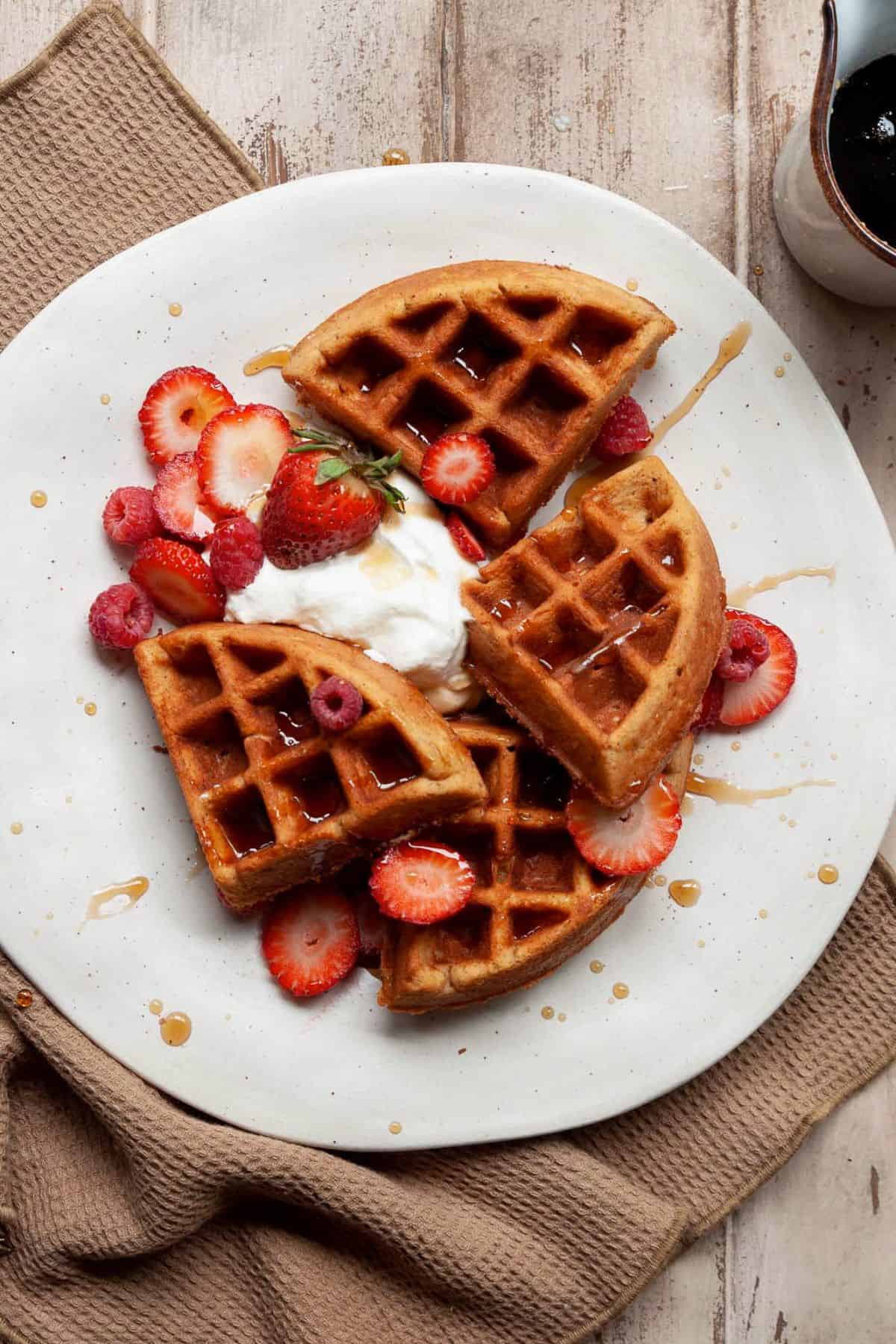 High-protein almond flour waffles topped with fresh strawberries, whipped cream, and syrup.