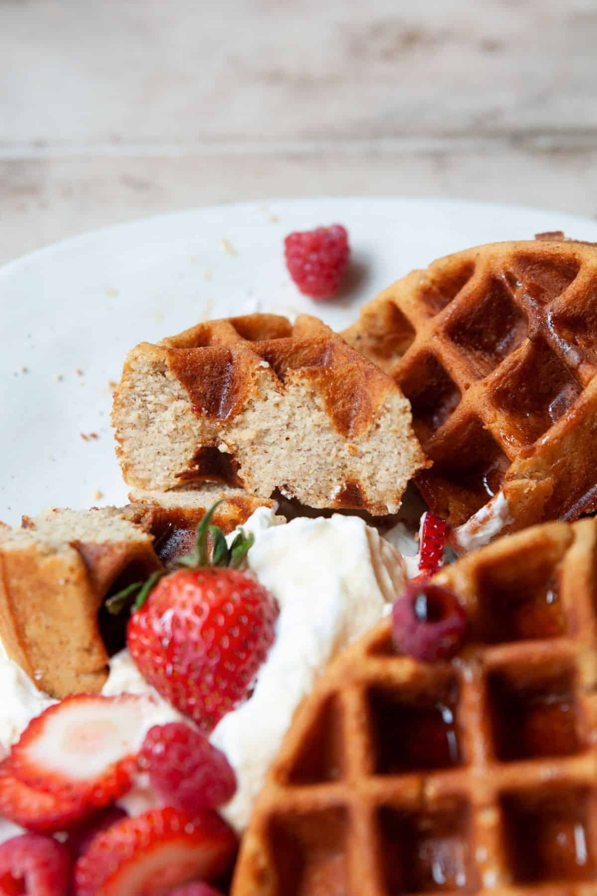 Close-up of a fluffy almond flour waffle showing the soft, tender interior with strawberries and whipped cream.