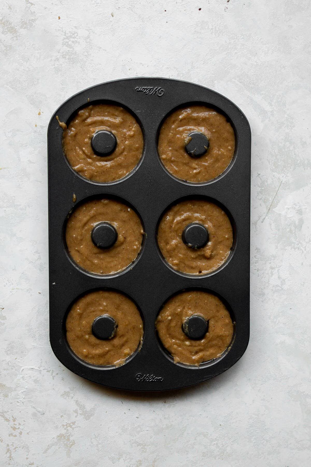 Banana donut batter spooned into a greased six-cavity donut pan.