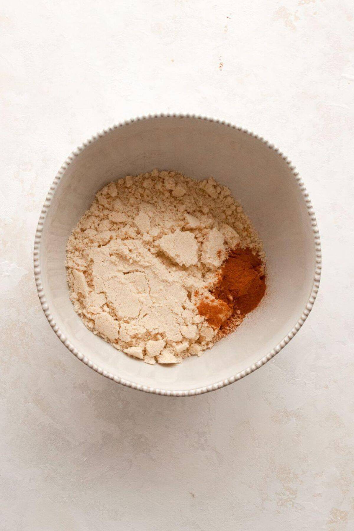 Whisking almond flour, oat flour, cinnamon, baking powder, and salt together in a white mixing bowl.