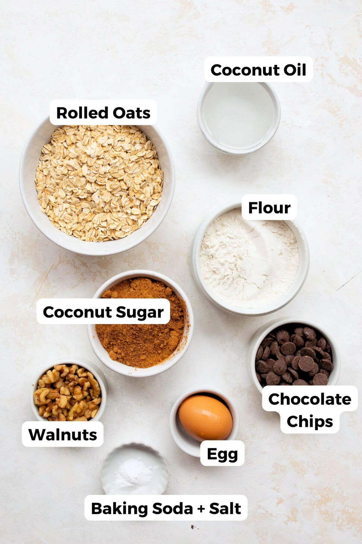 Ingredients for healthy oatmeal cookies: rolled oats, coconut oil, coconut sugar, flour, walnuts, chocolate chips, egg, baking soda.