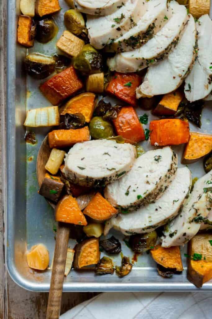 sliced chicken on a baking sheet with roasted veggies