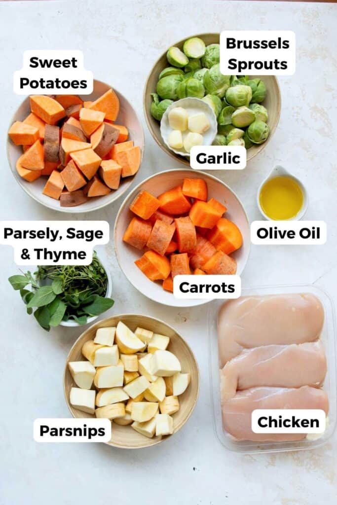 all ingredients in sheet pan chicken and veggies including chicken breast, carrots, garlic, sweet potatoes, Brussels sprouts, olive oil, and fresh herbs