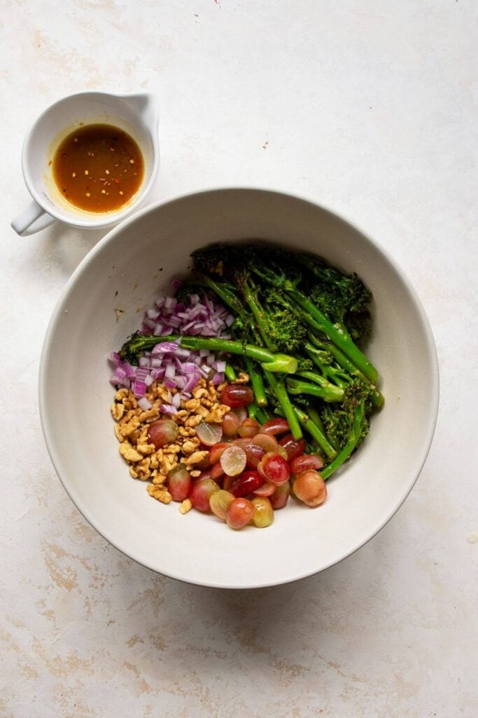 sautéed broccolini in a bowl with red onion, grapes, and walnuts