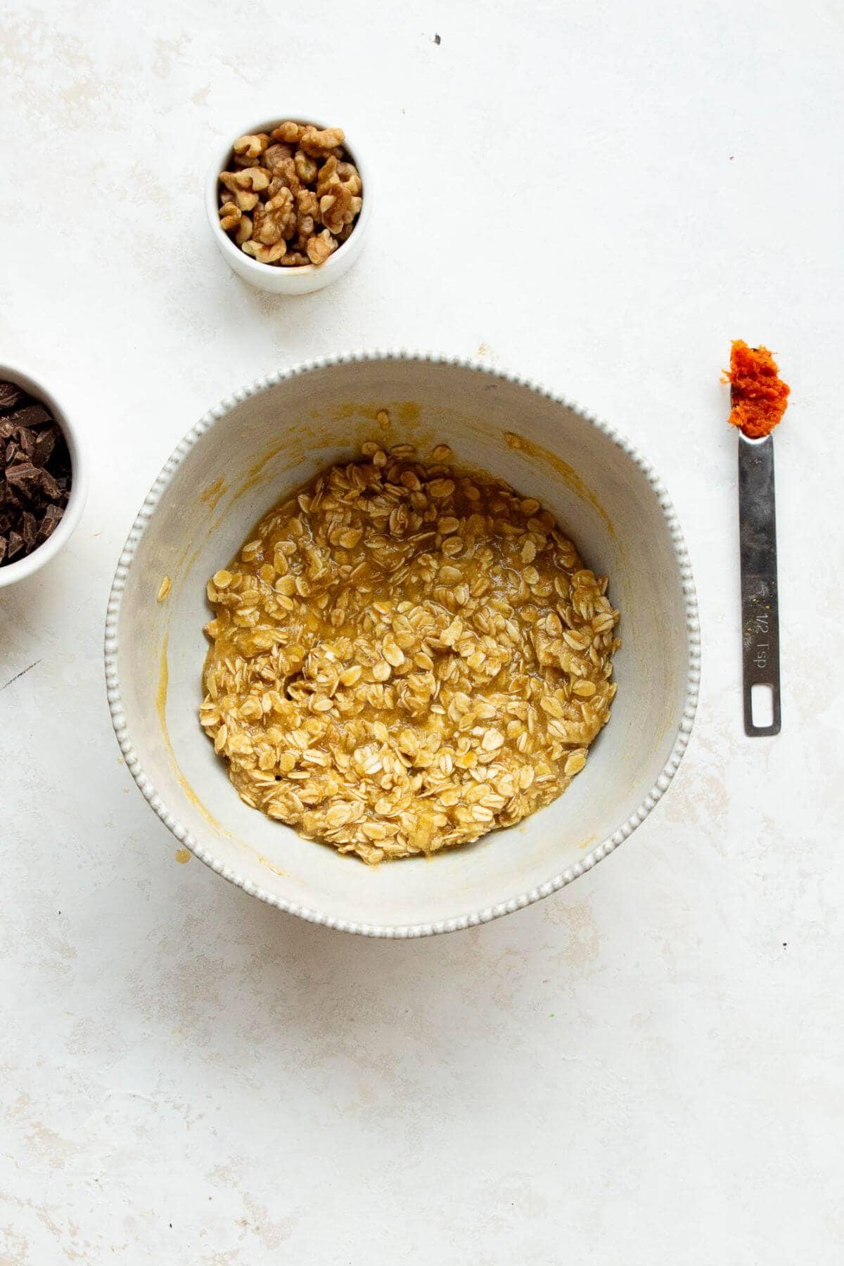 Oats and almond flour stirred into the wet ingredients, with orange zest on a spoon.