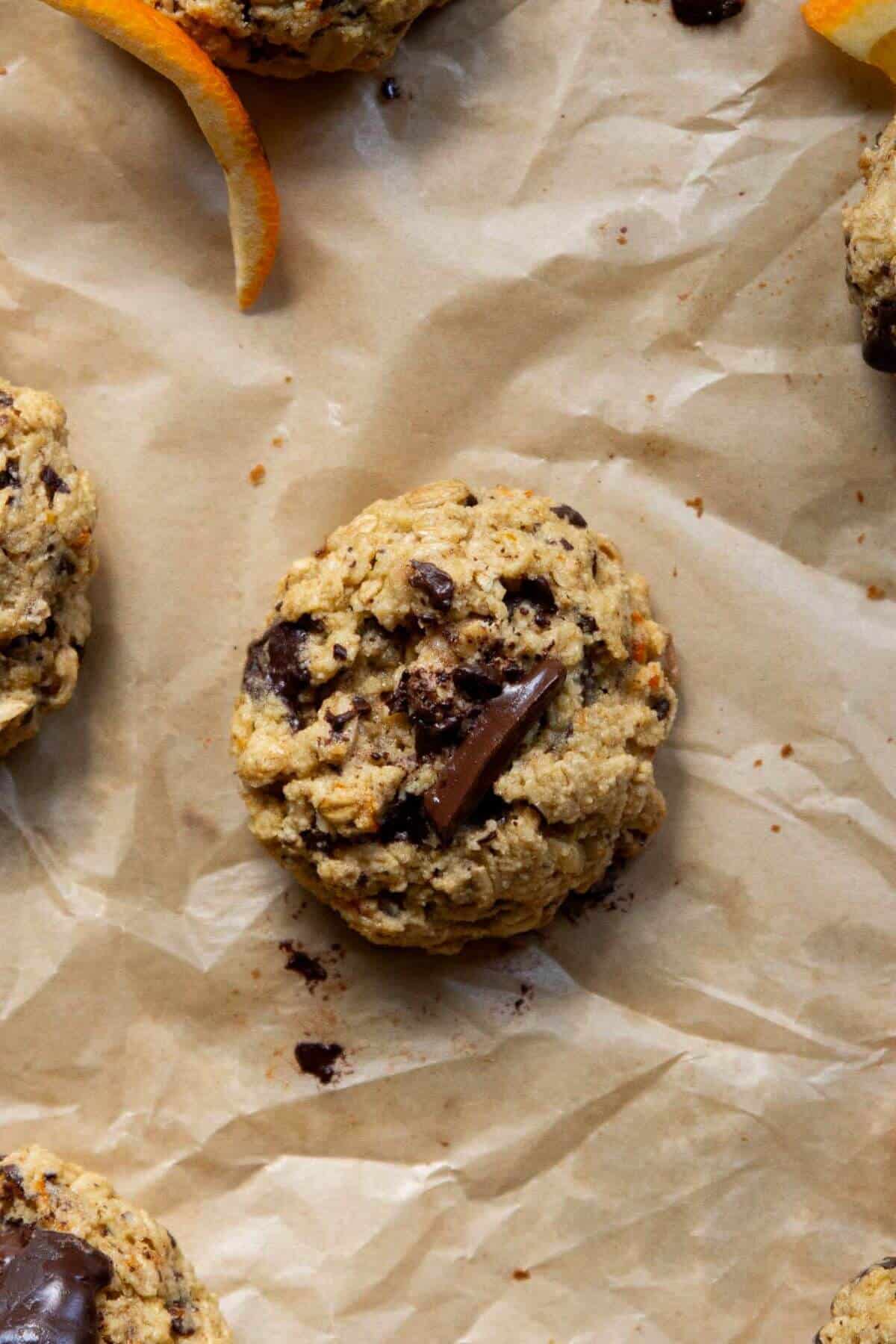 Orange chocolate chip oatmeal cookie with chocolate chunks on parchment paper.