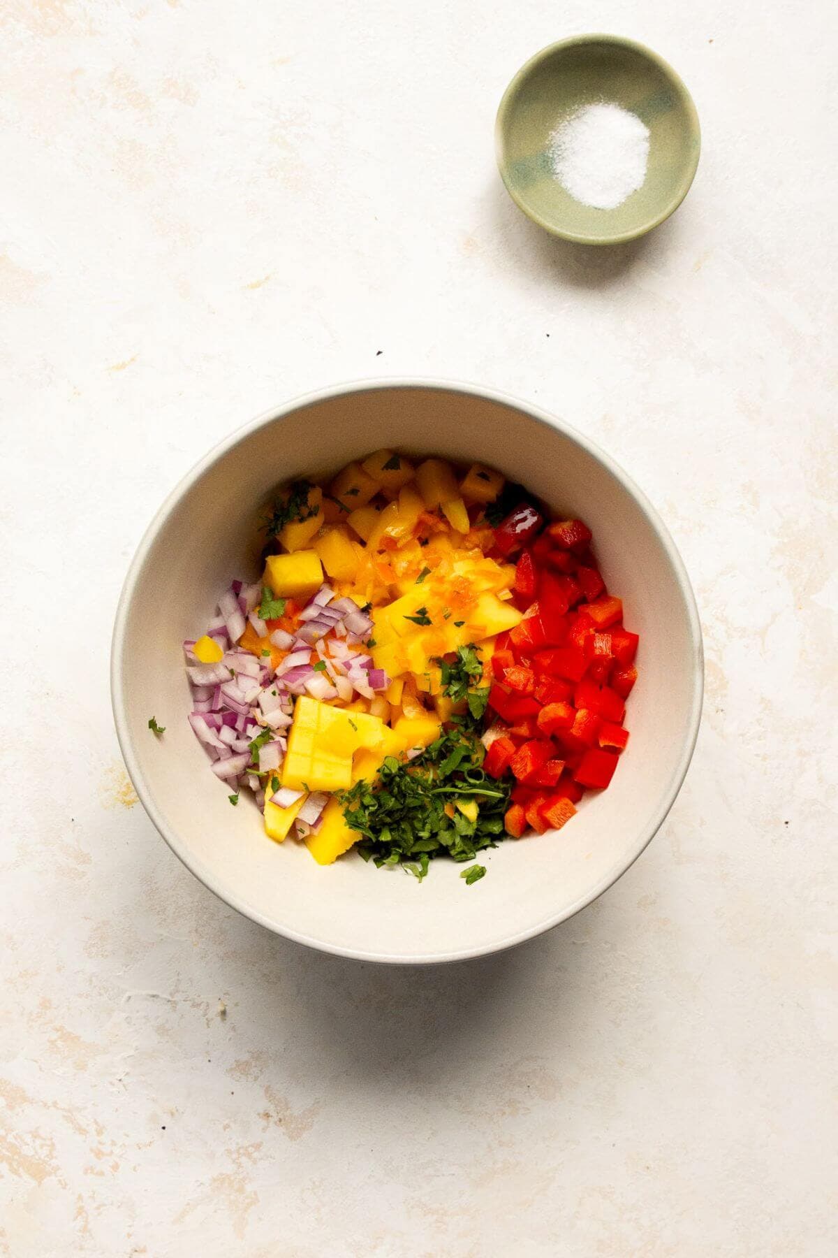 Diced mango, red bell pepper, onion, and cilantro in a bowl before mixing the salsa.