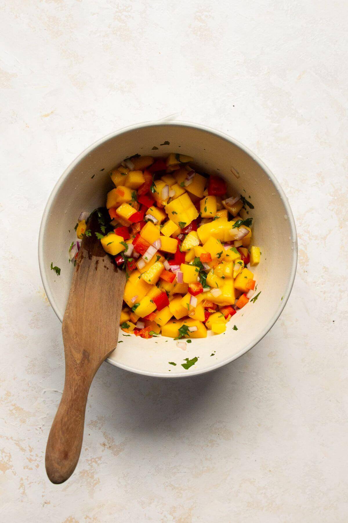 Mango habanero salsa being tossed together with a wooden spoon.