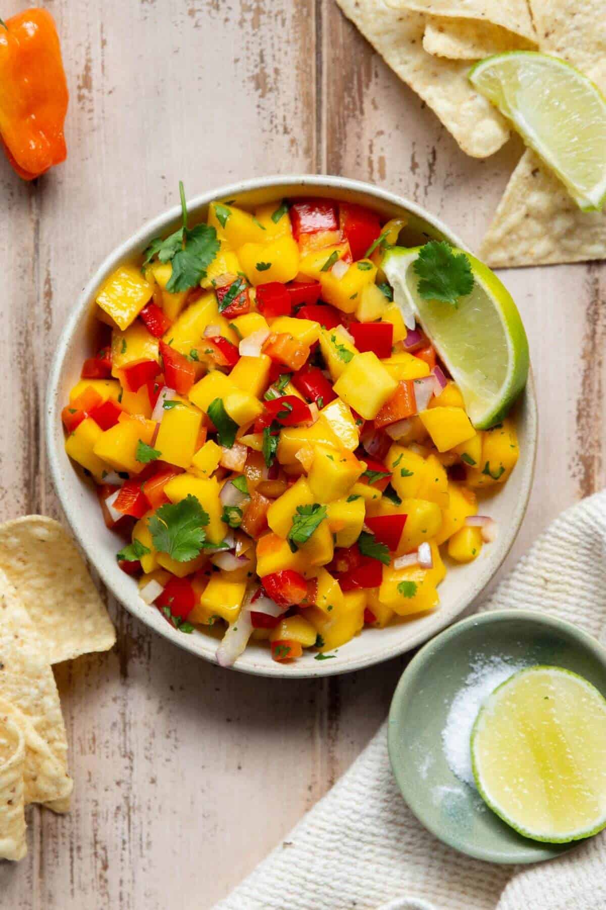 Spicy mango habanero salsa in a bowl with freshly mango, red bell pepper, and cilantro, served with tortilla chips and lime.