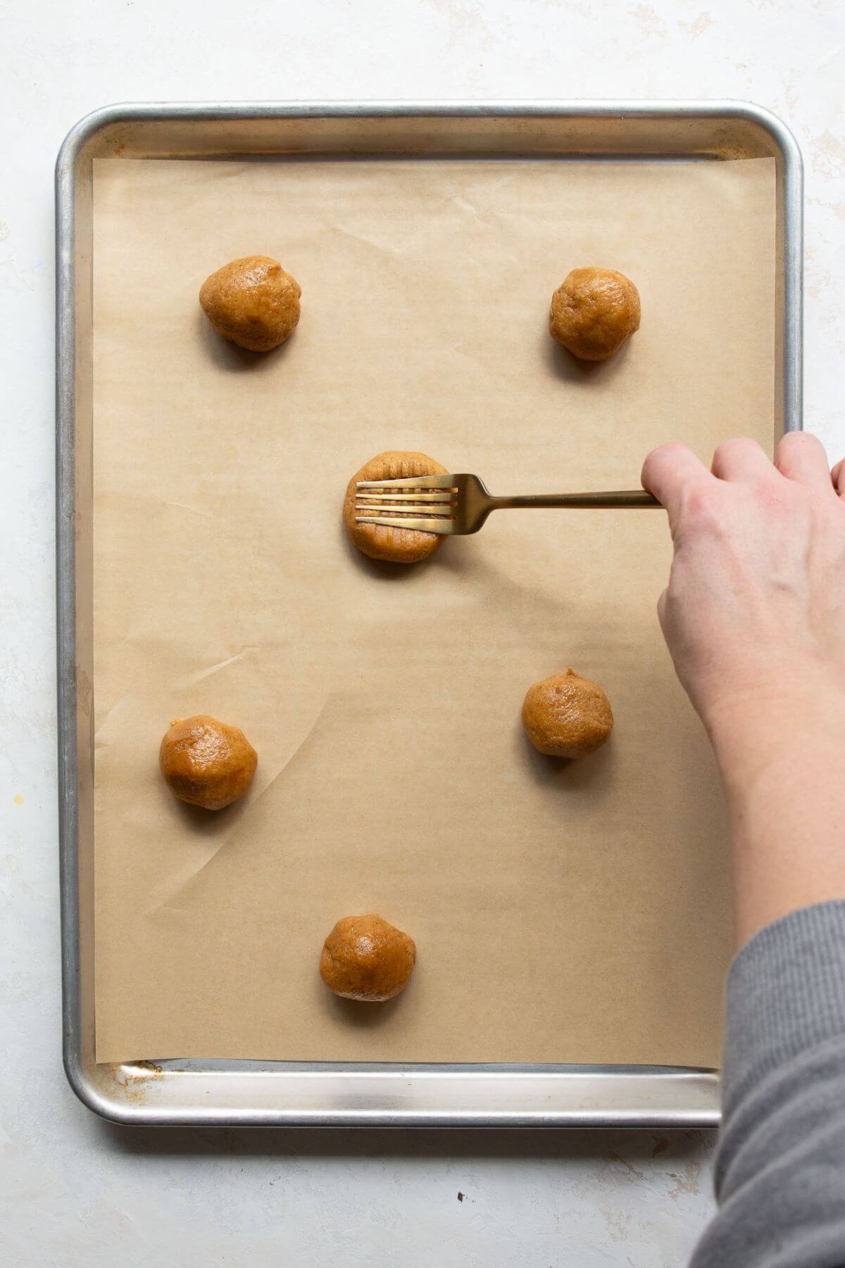 Using a fork to press a crisscross pattern into almond flour peanut butter cookie dough on a baking sheet.