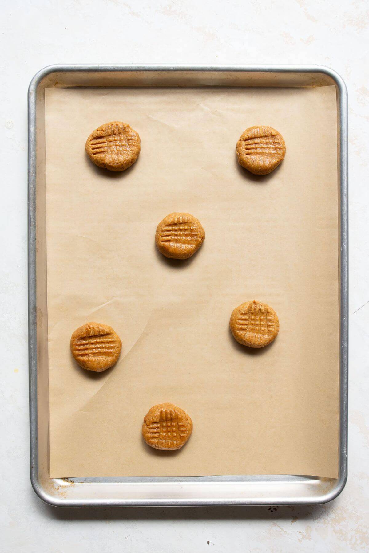 Unbaked almond flour peanut butter cookie dough with fork marks arranged on a parchment-lined baking sheet.