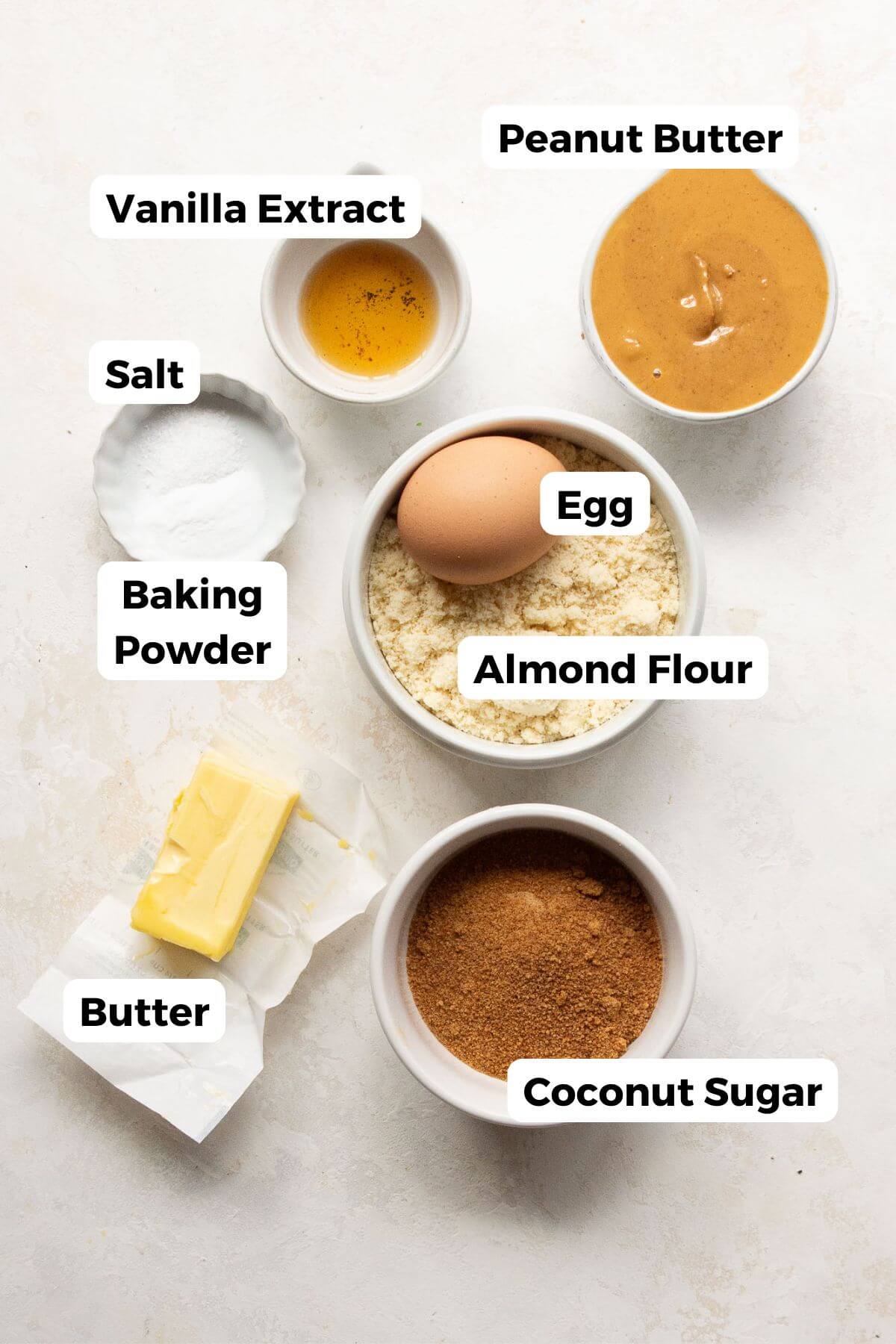 Ingredients for almond flour peanut butter cookies arranged in bowls, including almond flour, peanut butter, coconut sugar, butter, egg, vanilla, salt, and baking powder.