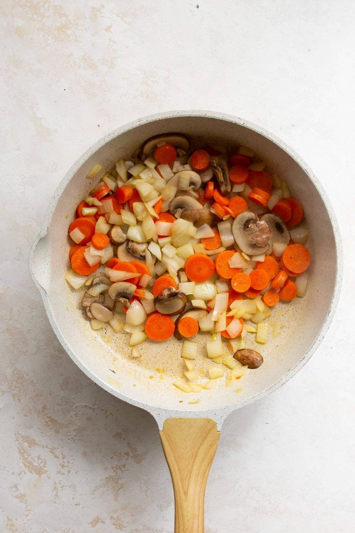 Sautéing mushrooms, onions, carrots and garlic in a pan