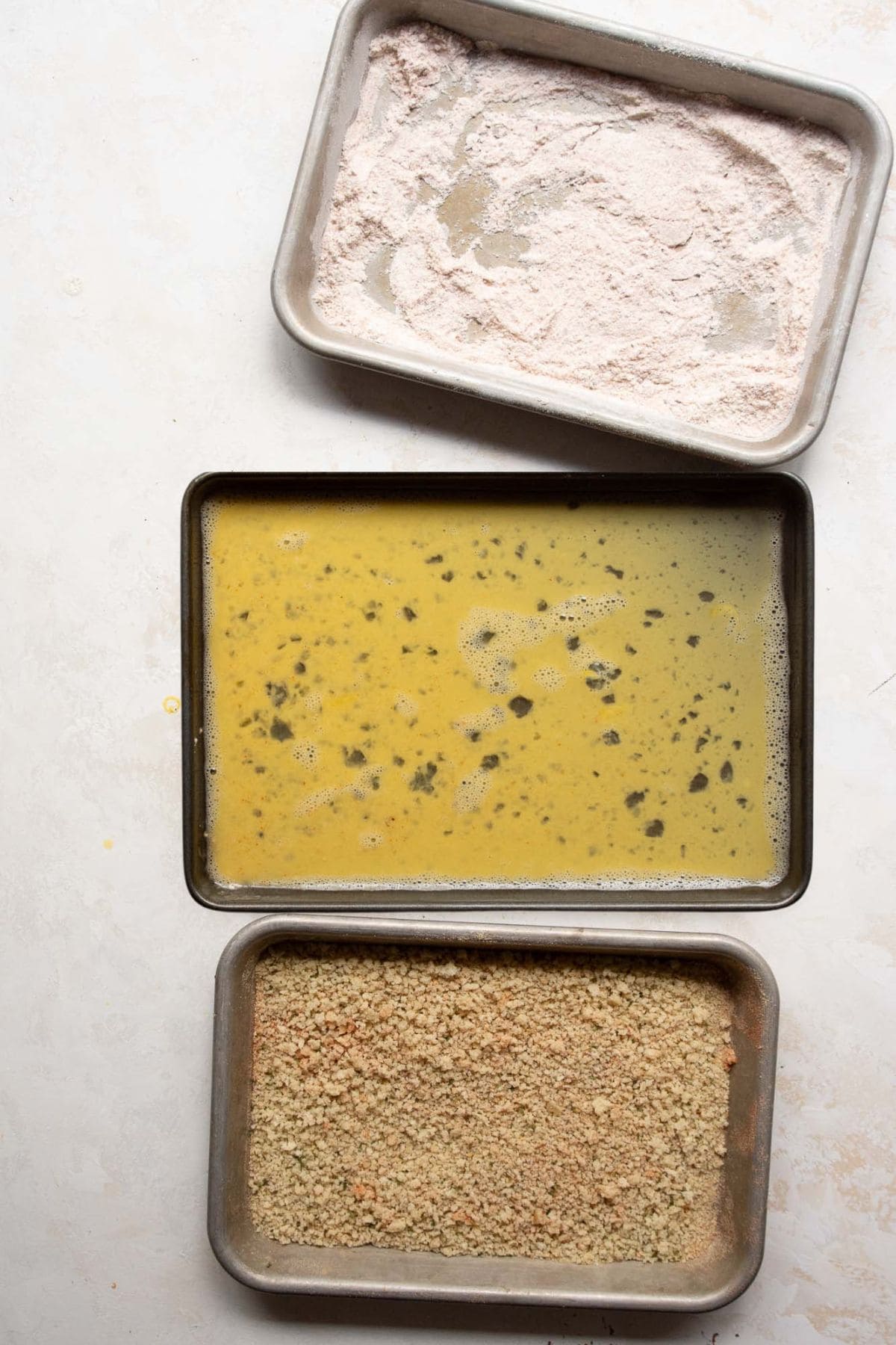 Three bowls for coating chicken cutlets: one with flour and seasonings, one with whisked eggs, and one with the breadcrumbs and remaining seasonings.