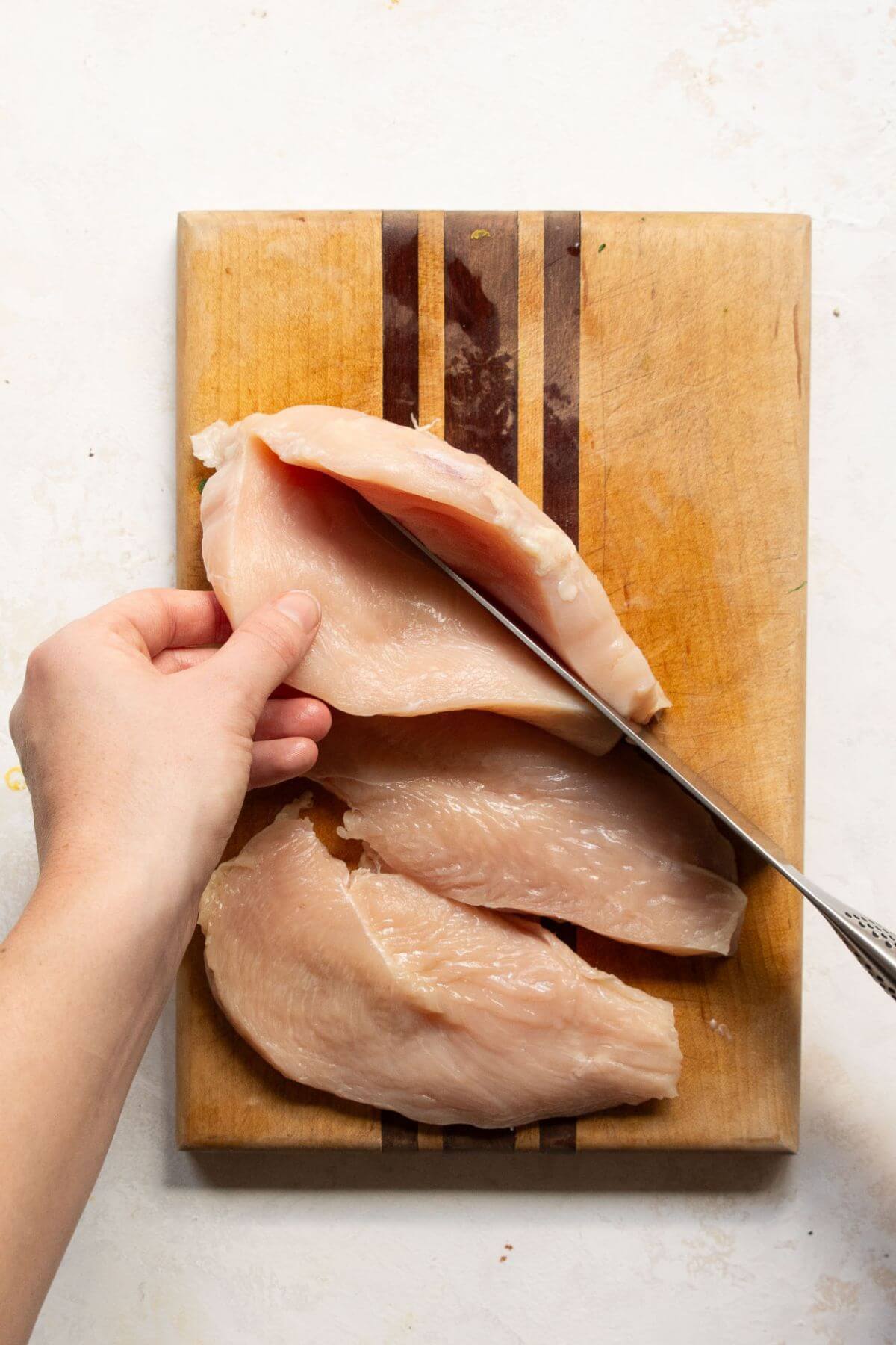 Slicing a chicken breast in half to make thin chicken cutlets.