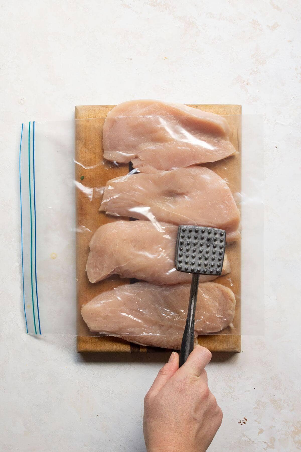 Pounding butterflied chicken halves with a mallet to make it thin.
