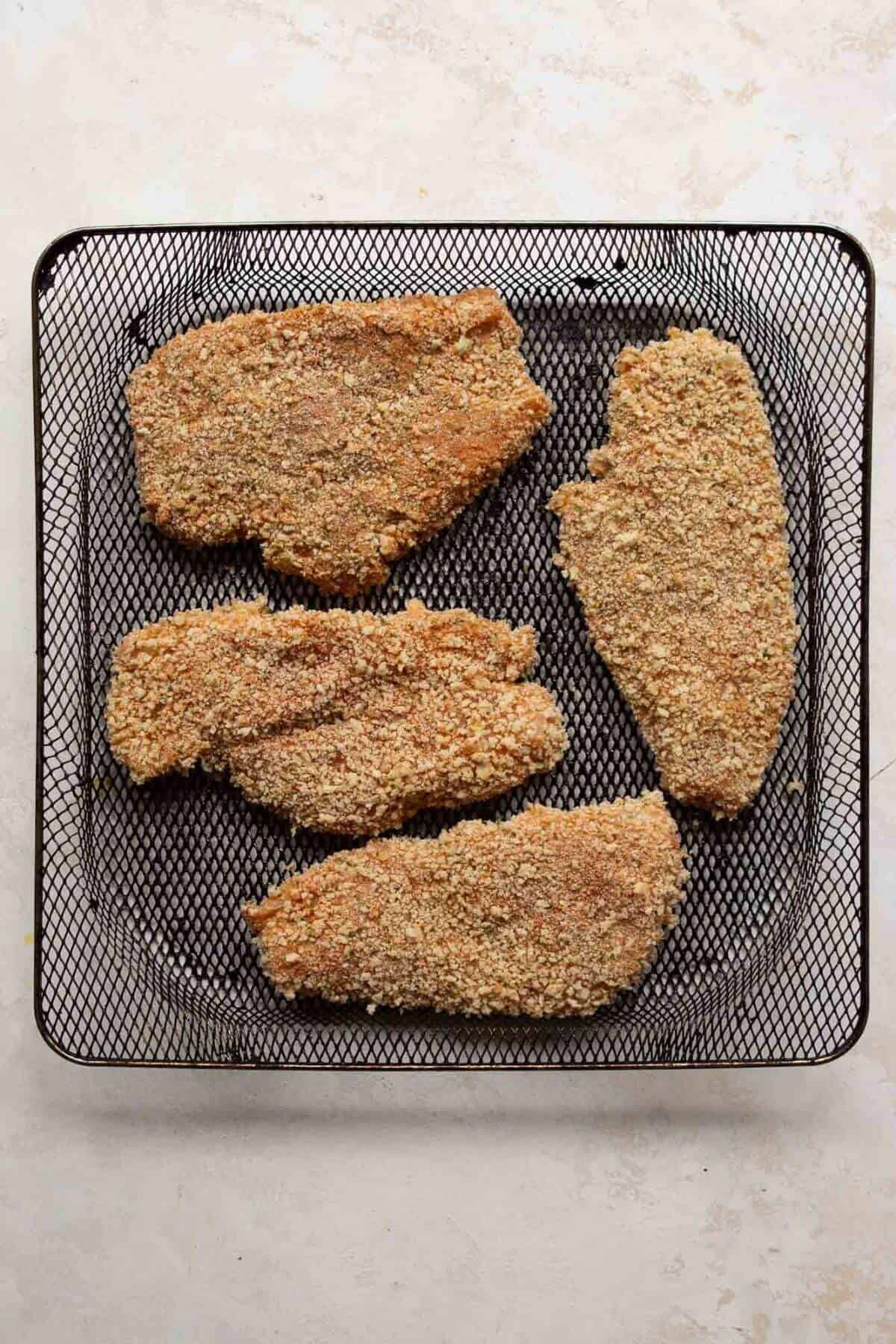 Uncooked breaded chicken cutlets in air fryer basket.