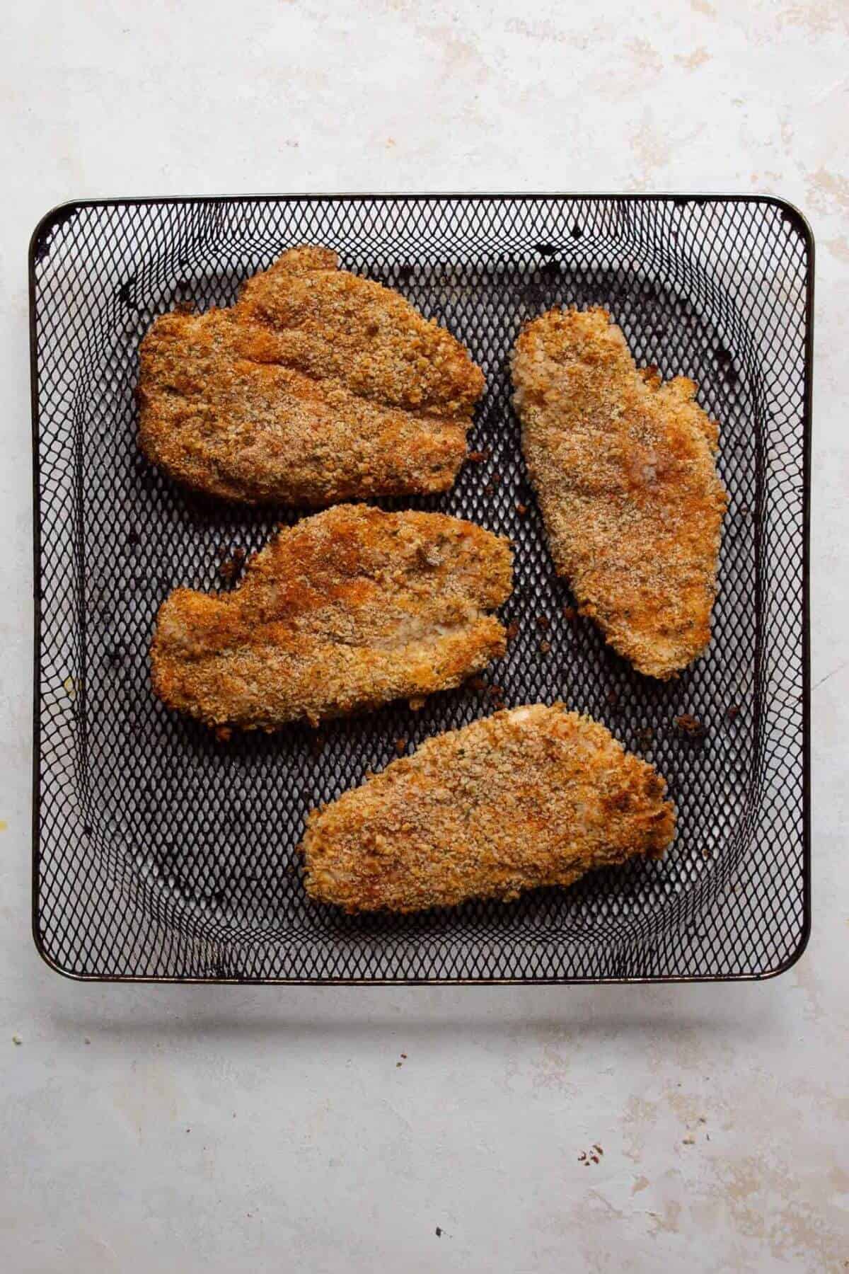 Crispy and golden breaded chicken cutlets in air fryer basket.