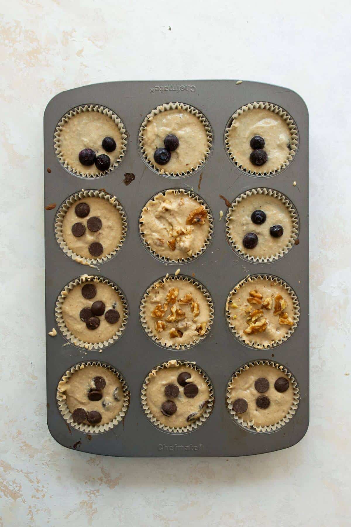 unbaked oatmeal banana muffins in a tin. One row with blueberries, one with chocolate chips, and one with walnuts