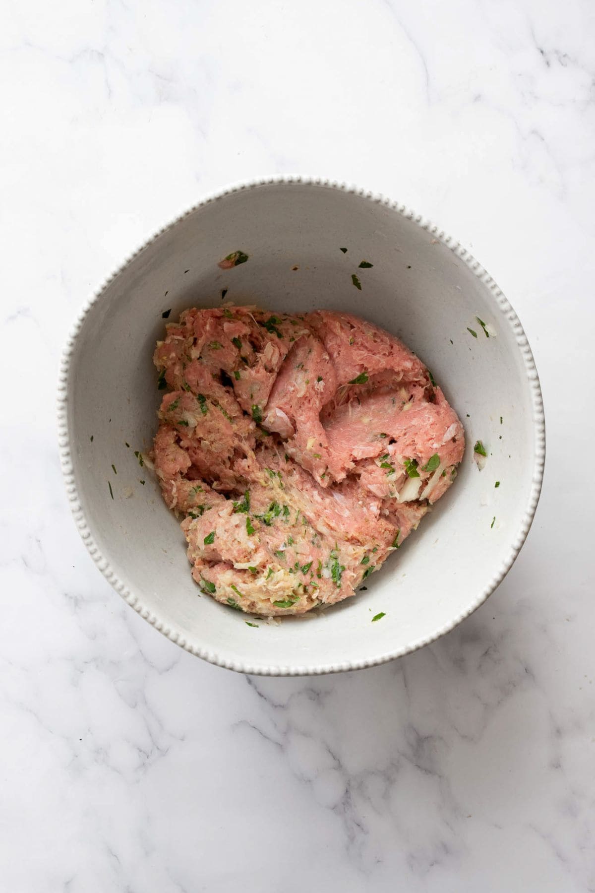 Mixed ground turkey burger mixture in a white bowl, seasoned and ready to form into patties.
