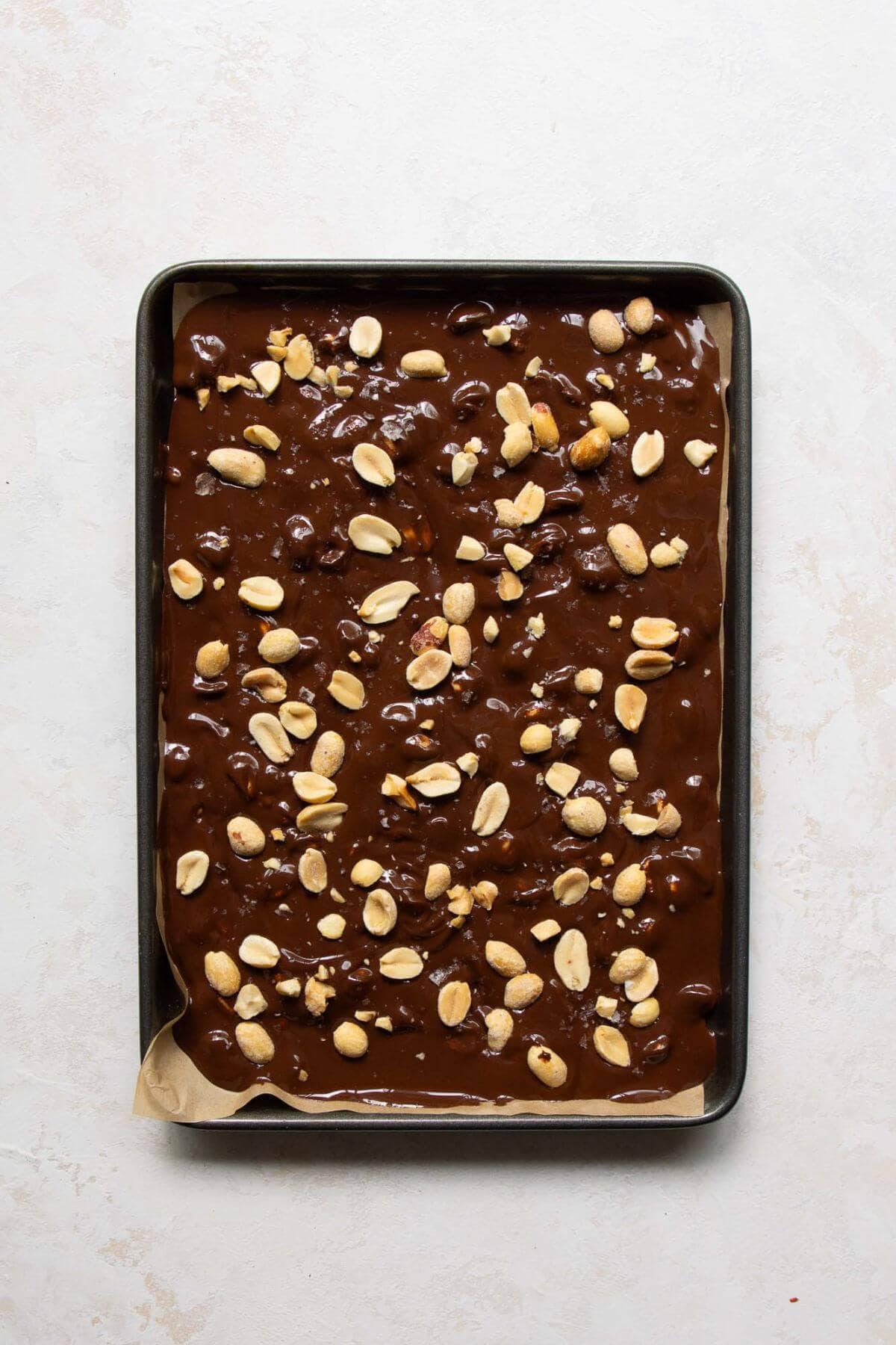 melted dark chocolate on a baking sheet with roasted peanuts