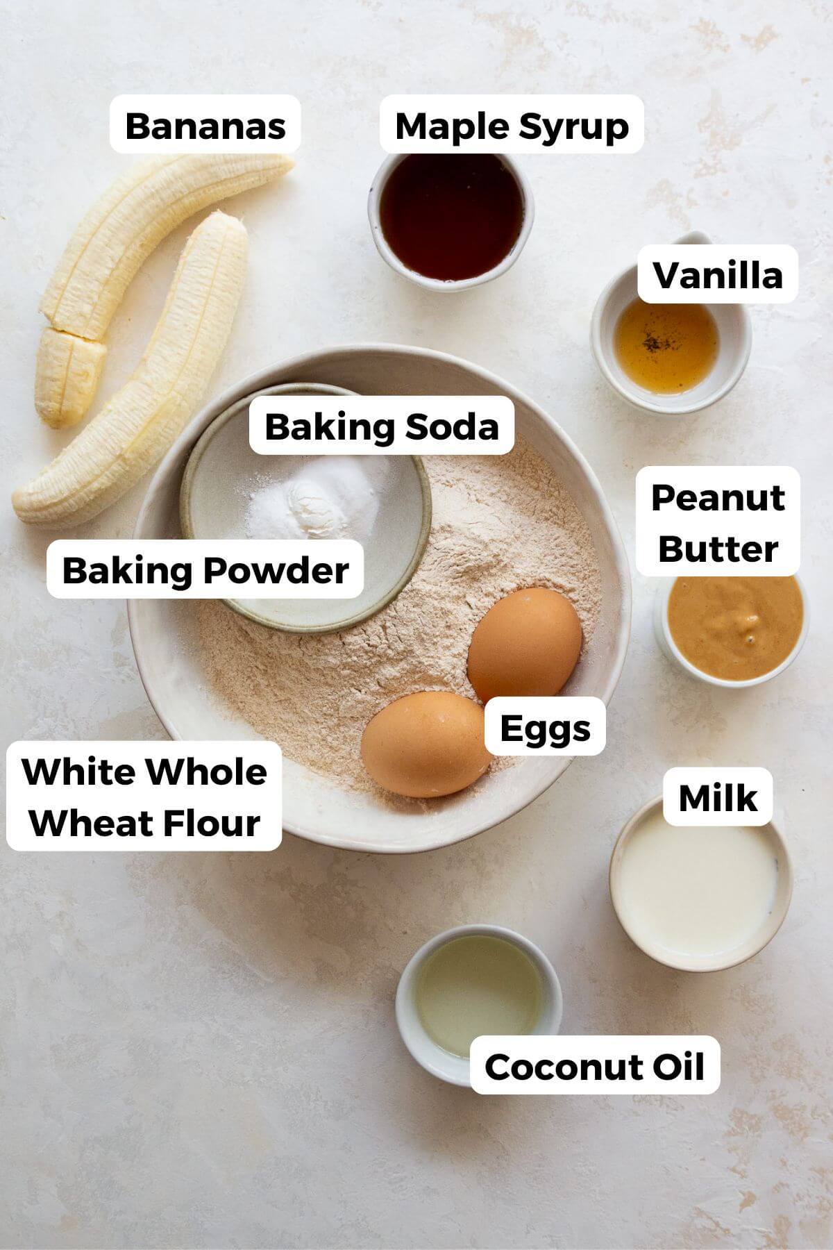 all ingredients in healthy peanut butter banana bread in bowls including banana, peanut butter, maple syrup, vanilla, peanut butter, baking soda, baking powder, white whole wheat flour, milk, and coconut oil