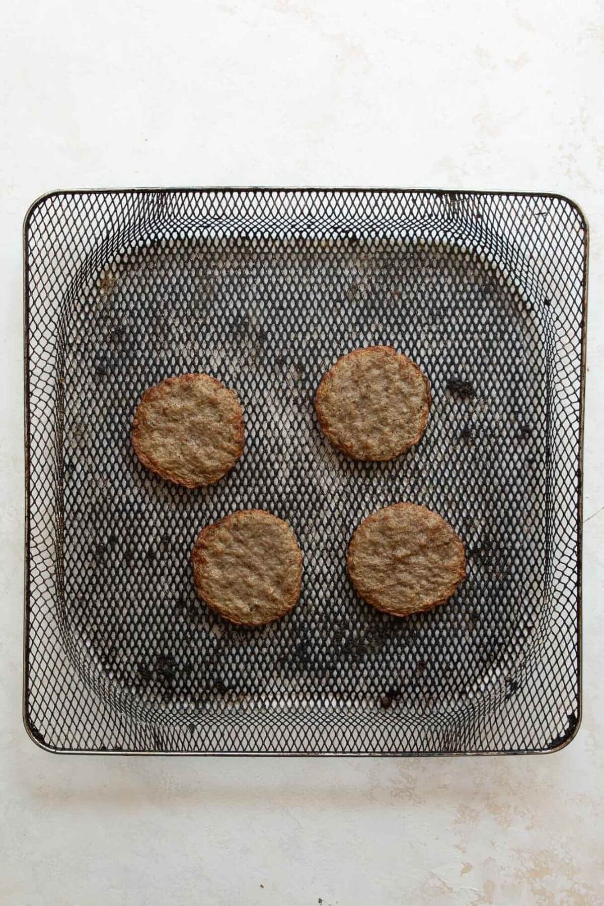 four crispy, golden brown sausage patties in an air fryer basket