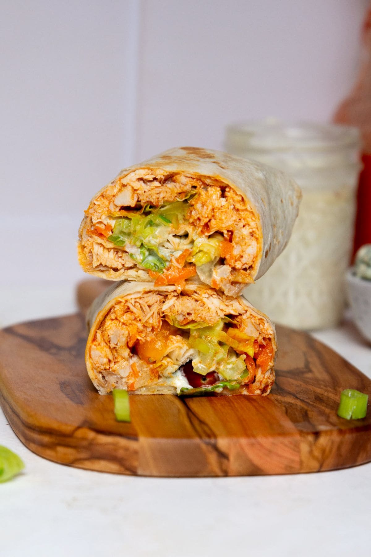 Sliced healthy buffalo chicken wraps showing the saucy and creamy filling with chicken, lettuce, avocado, and yogurt caesar dressing.
