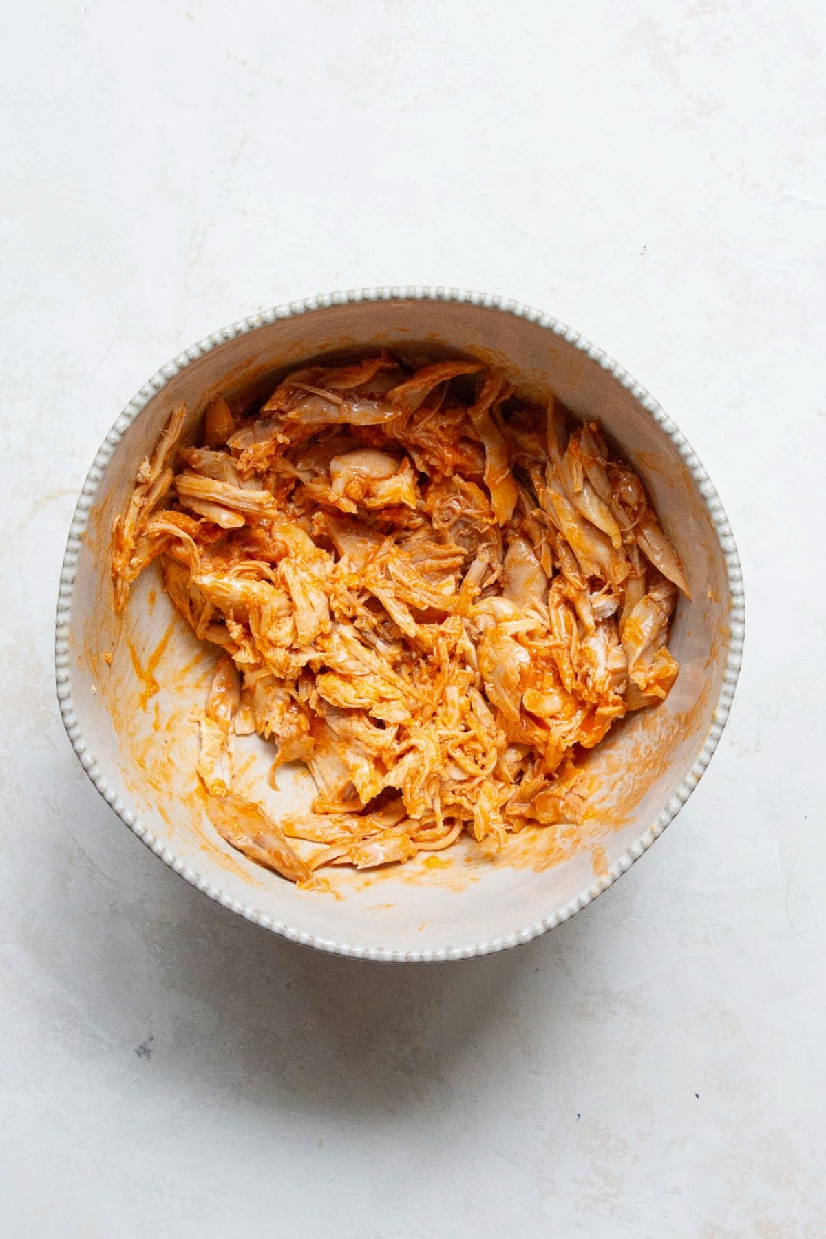 Shredded rotisserie chicken in a bowl tossed with buffalo sauce.