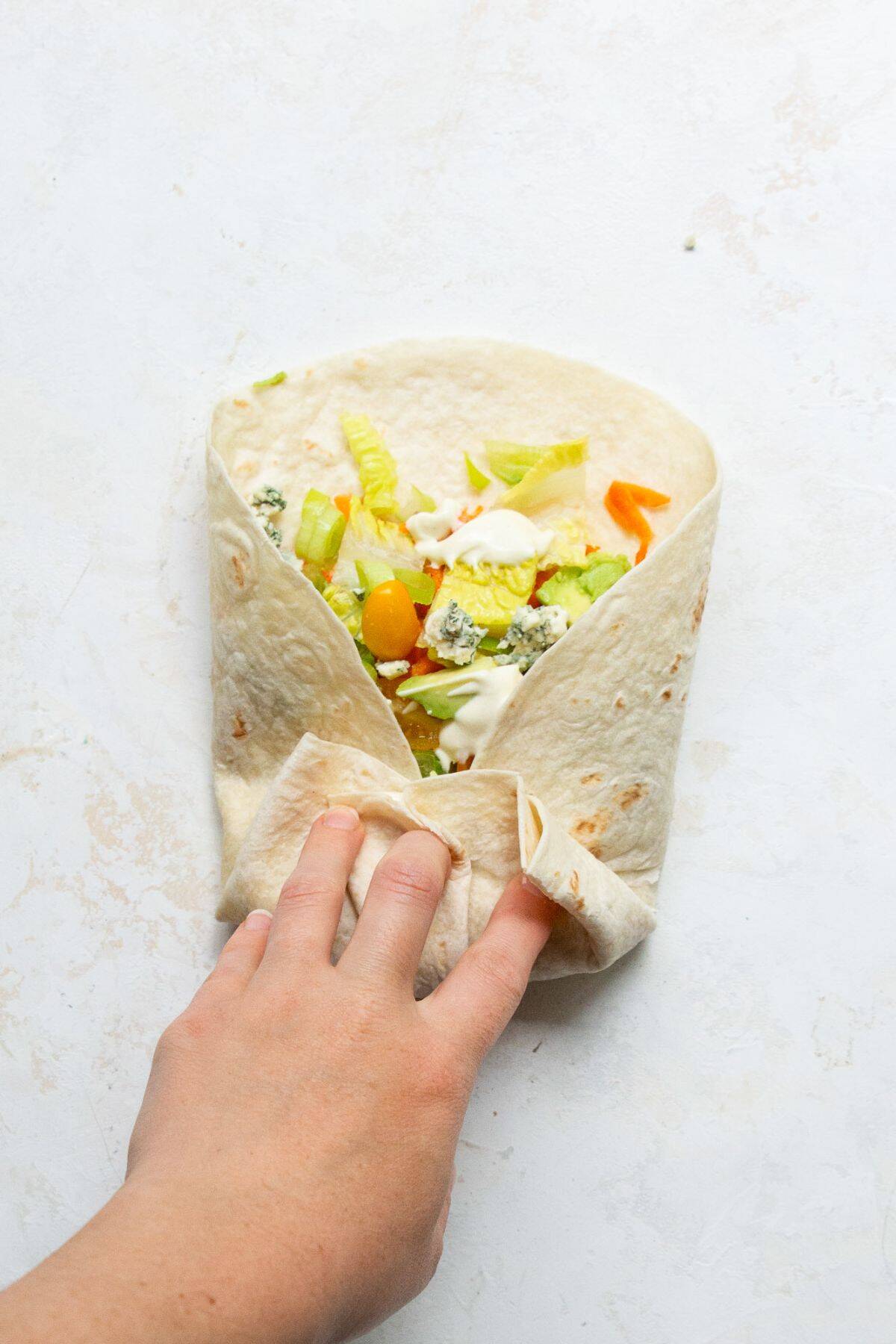 Step-by-step wrapping of a healthy buffalo chicken Caesar wrap burrito-style, with hands folding the tortilla.