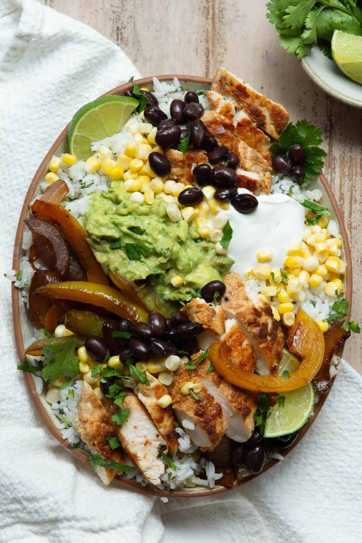 Assembled healthy chicken fajita bowl with blackened chicken, charred peppers, cilantro lime rice, black beans, corn, guacamole, and sour cream.