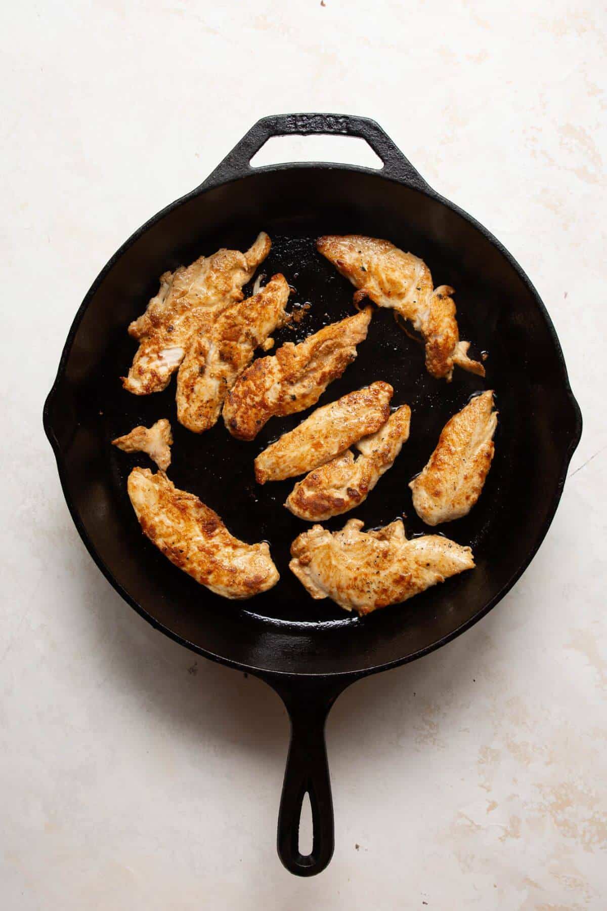 Blackened chicken tenders cooking in a cast iron skillet for high protein chicken fajita bowls.