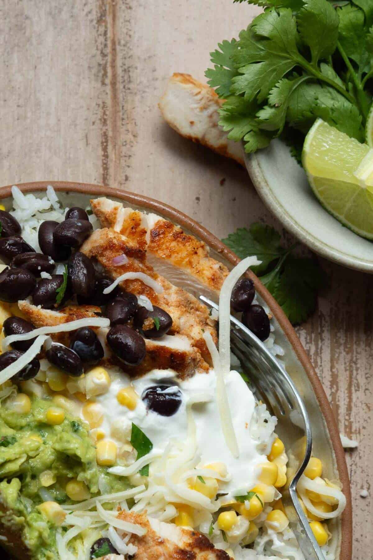 Healthy high protein chicken fajita bowl with blackened chicken, homemade guacamole, black beans, corn, and cilantro lime rice.