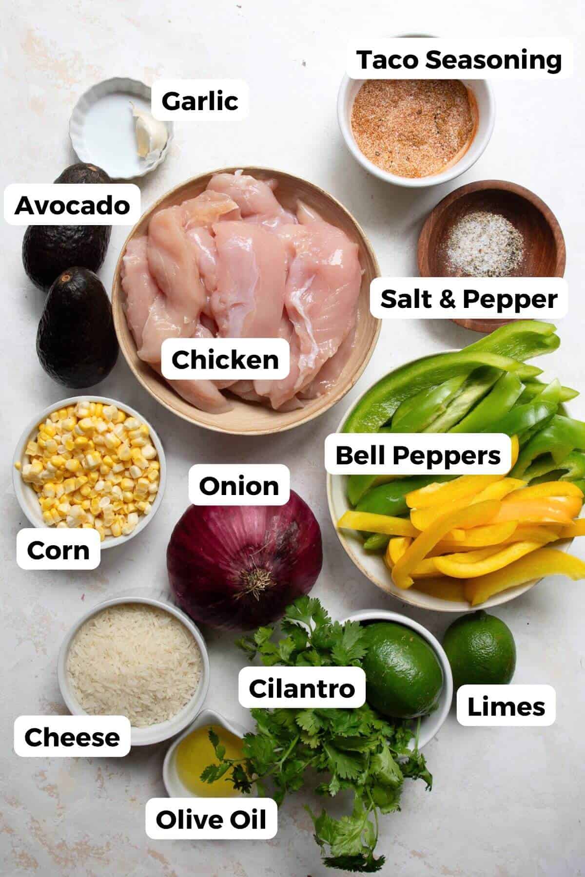 Ingredients for healthy chicken fajita bowls including chicken, bell peppers, onion, avocado, corn, cilantro, limes, cheese, and olive oil.