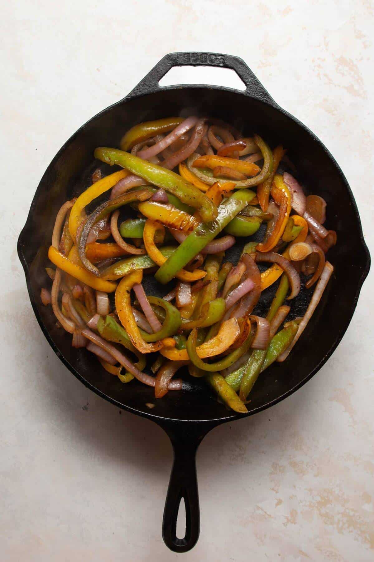 Charred bell peppers and red onions sautéed in a cast iron skillet for healthy chicken fajita bowls.