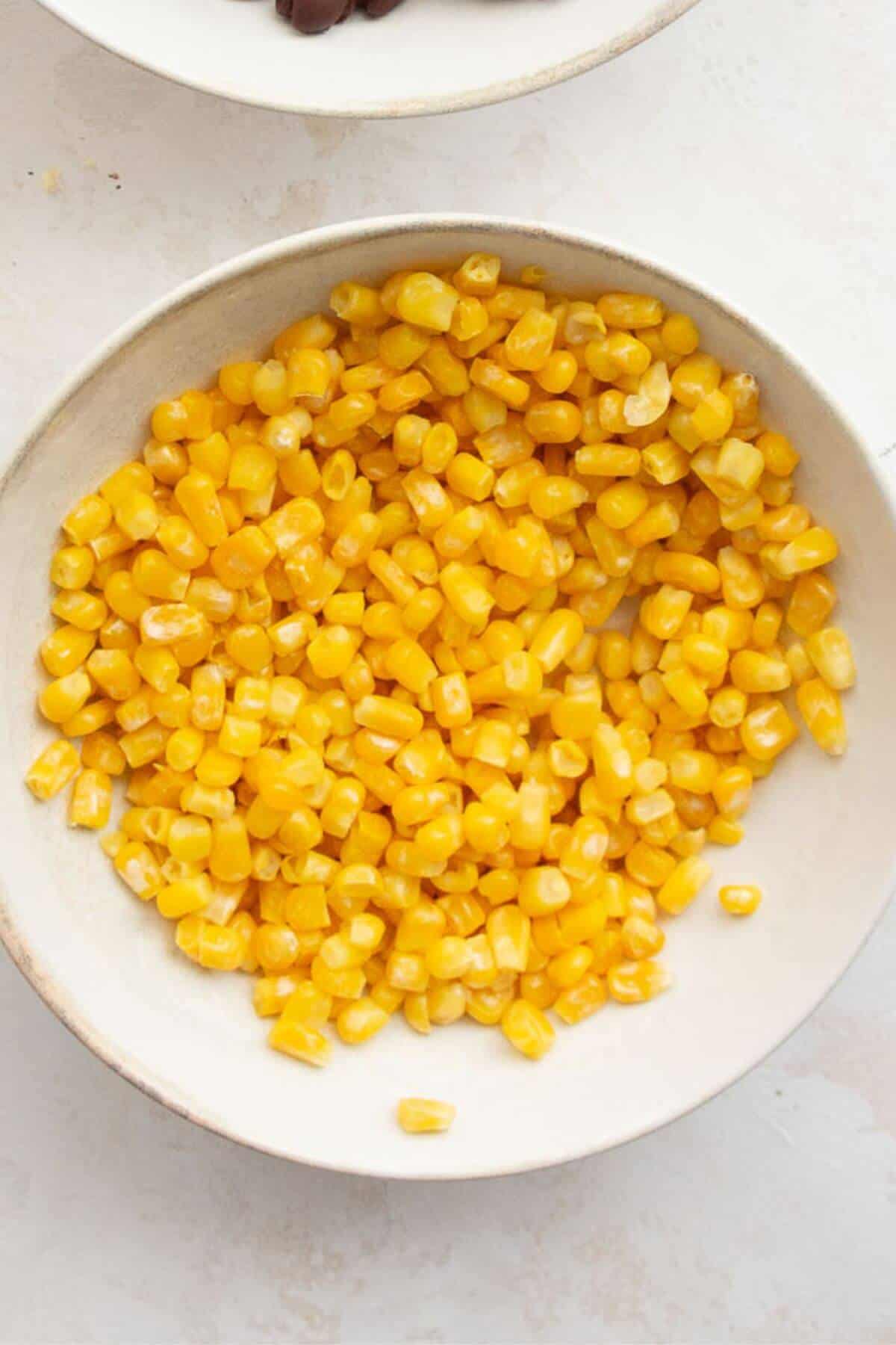 Frozen corn heated and seasoned with salt and pepper for healthy chicken fajita meal prep bowls.