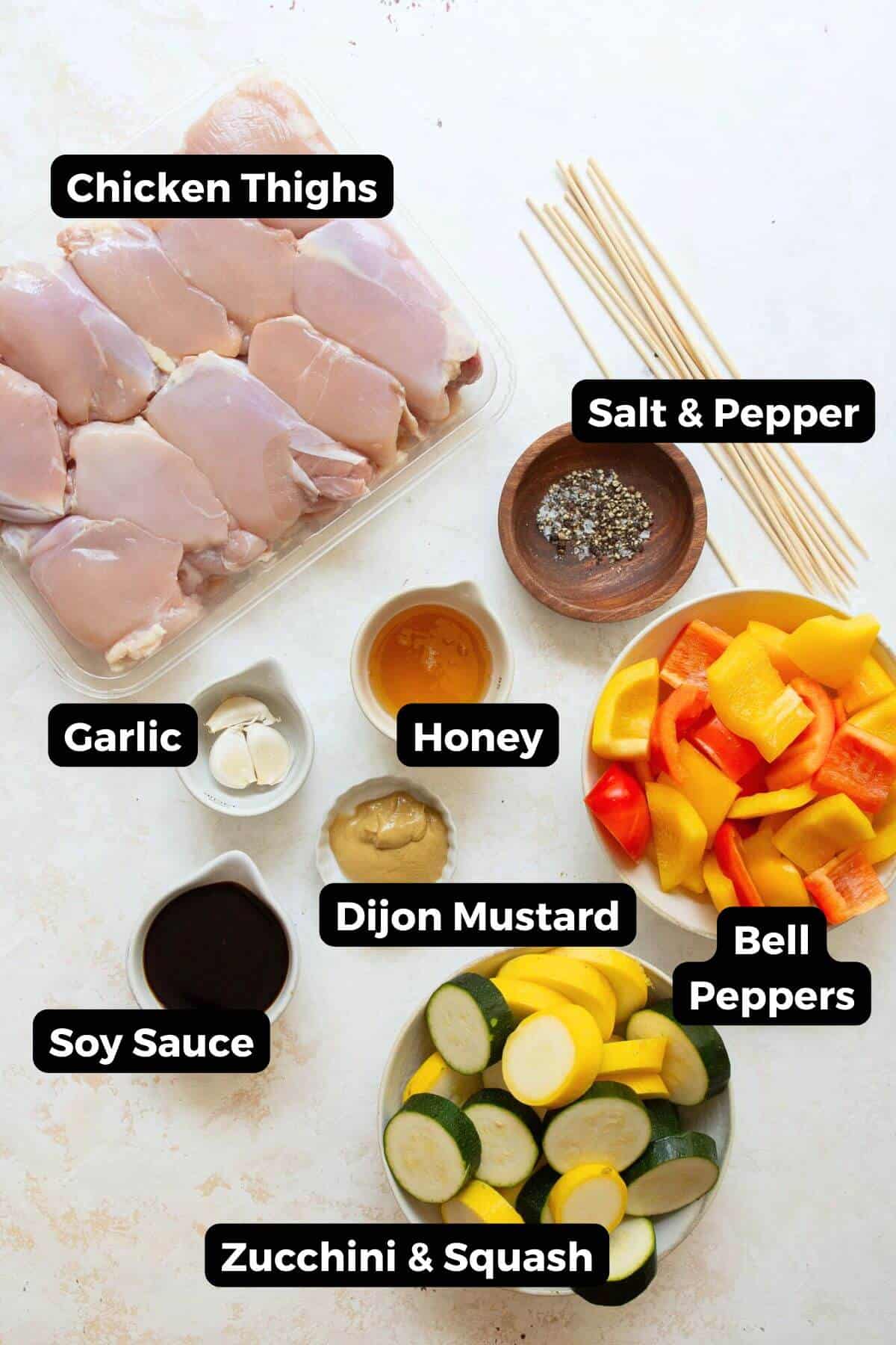 Ingredients for honey soy chicken kebabs, including raw chicken thighs, bell peppers, zucchini, red onion, garlic, honey, soy sauce, and mustard.