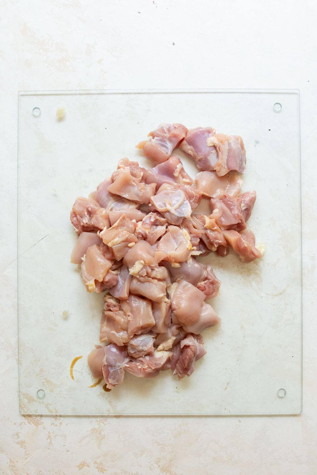 Trimming excess fat off raw boneless chicken thighs on a cutting board