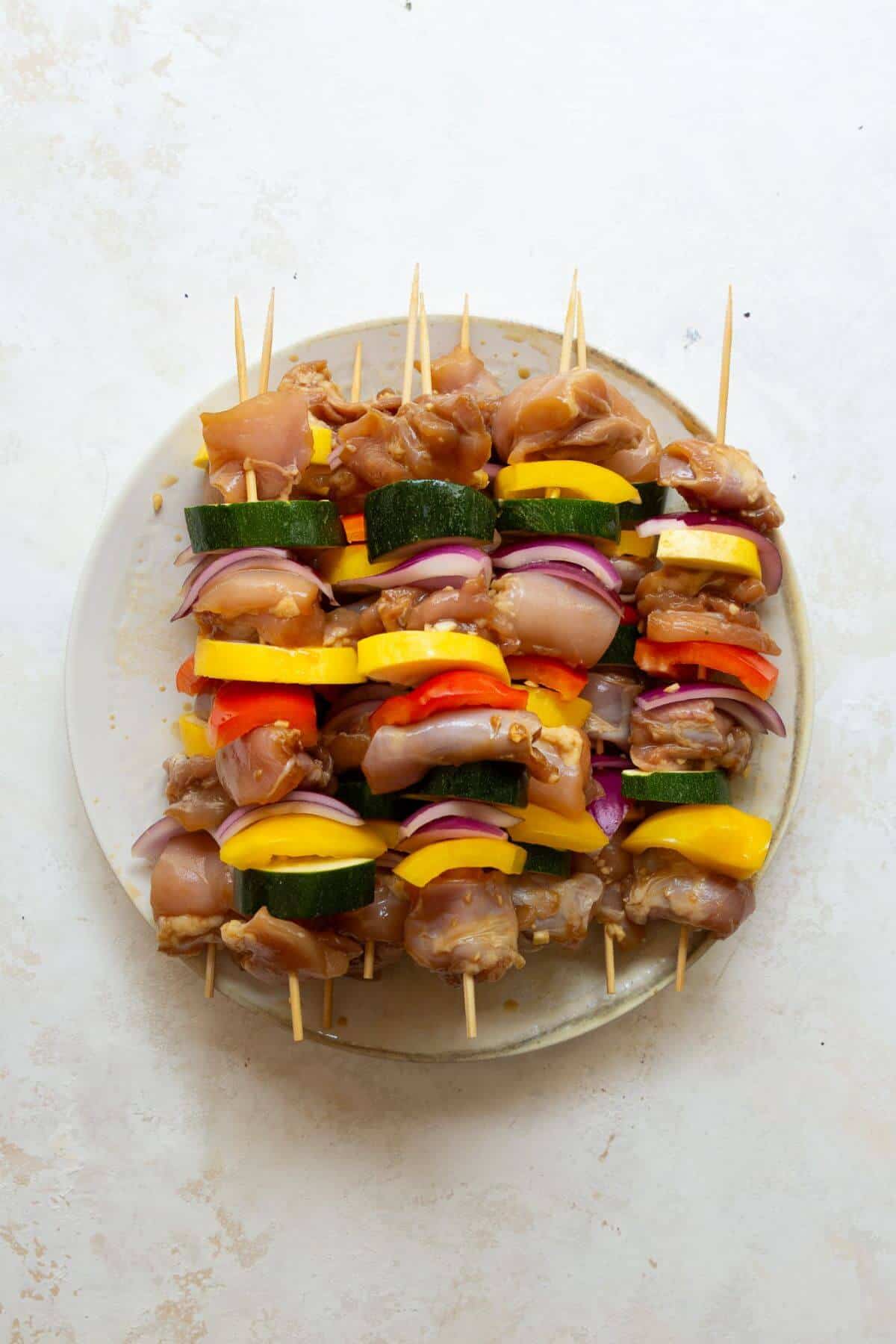 Uncooked chicken and vegetable skewers arranged on a plate, ready to be grilled