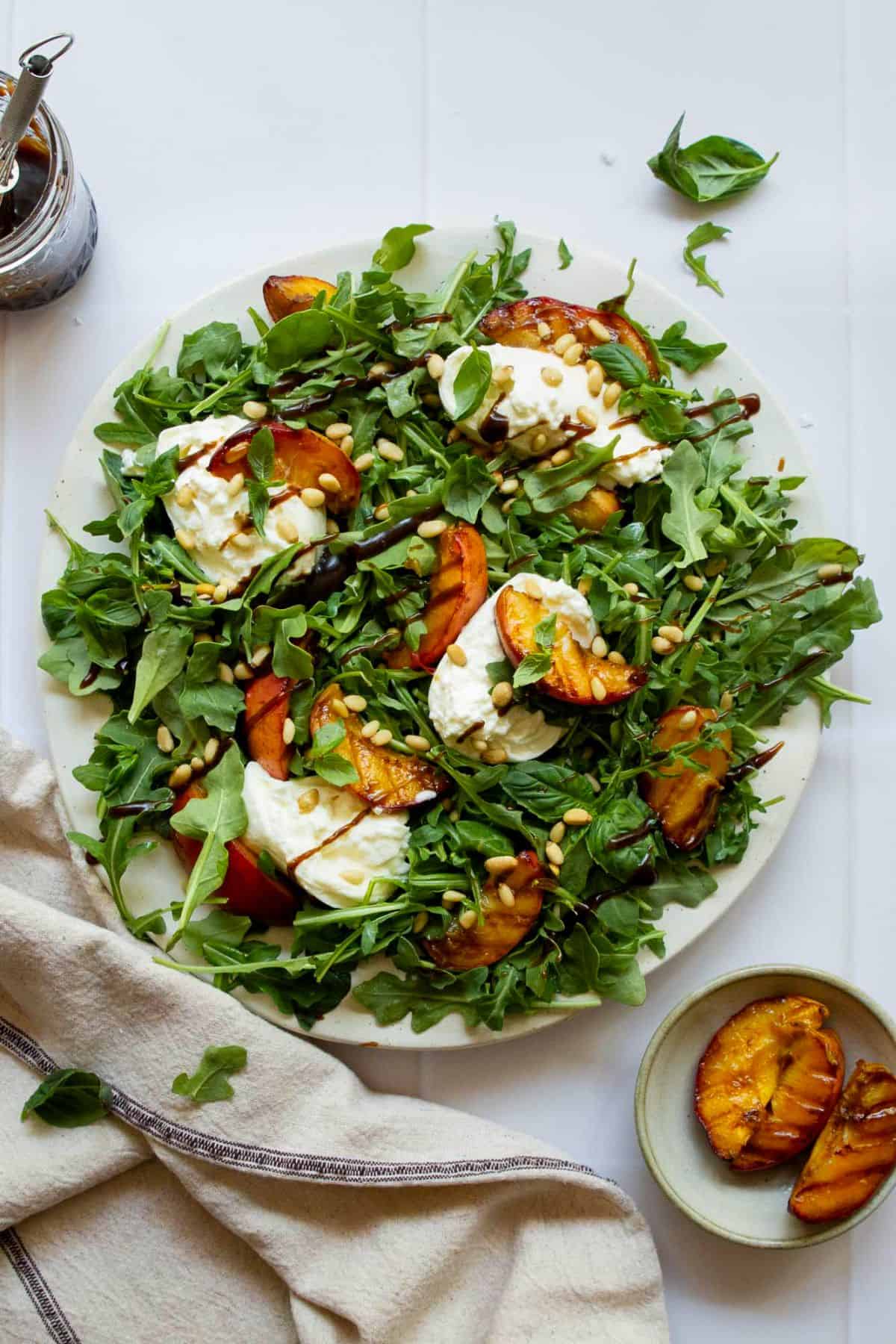 Summer salad featuring grilled peaches, torn burrata cheese, basil leaves, and a drizzle of balsamic vinaigrette.