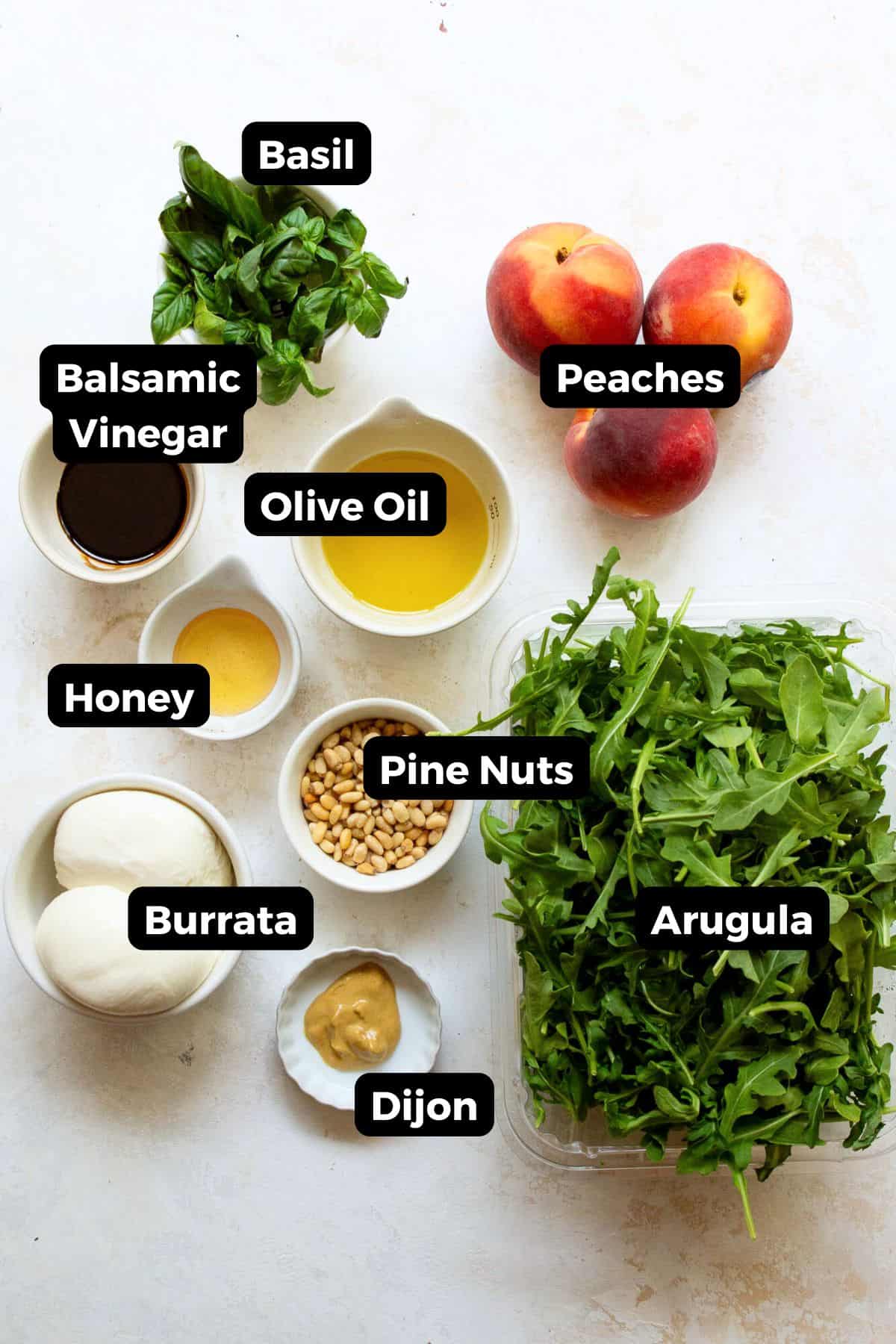 Overhead shot of salad ingredients in small bowls, including peaches, arugula, burrata cheese, fresh basil, pine nuts, olive oil, balsamic vinegar, honey, and Dijon mustard.