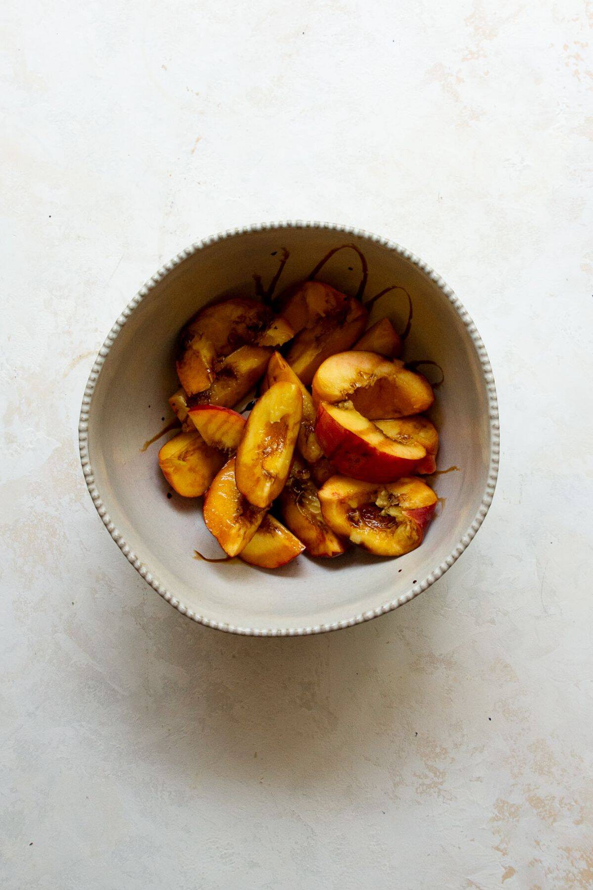 peach slices in a bowl marinating with balsamic vinegar and olive oil