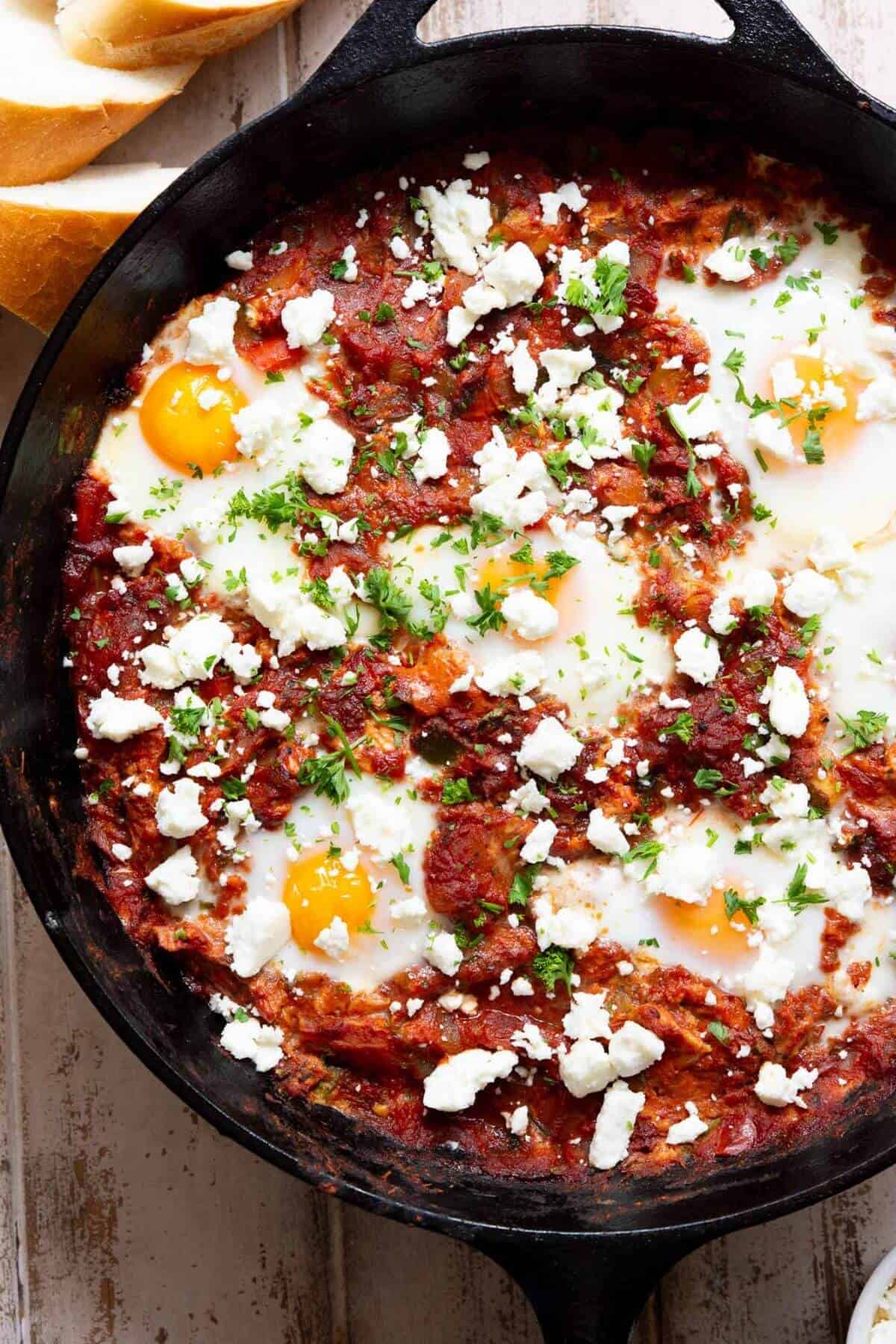 Healthy shakshuka with poached eggs, tomato sauce, and feta cheese served in a cast iron pan