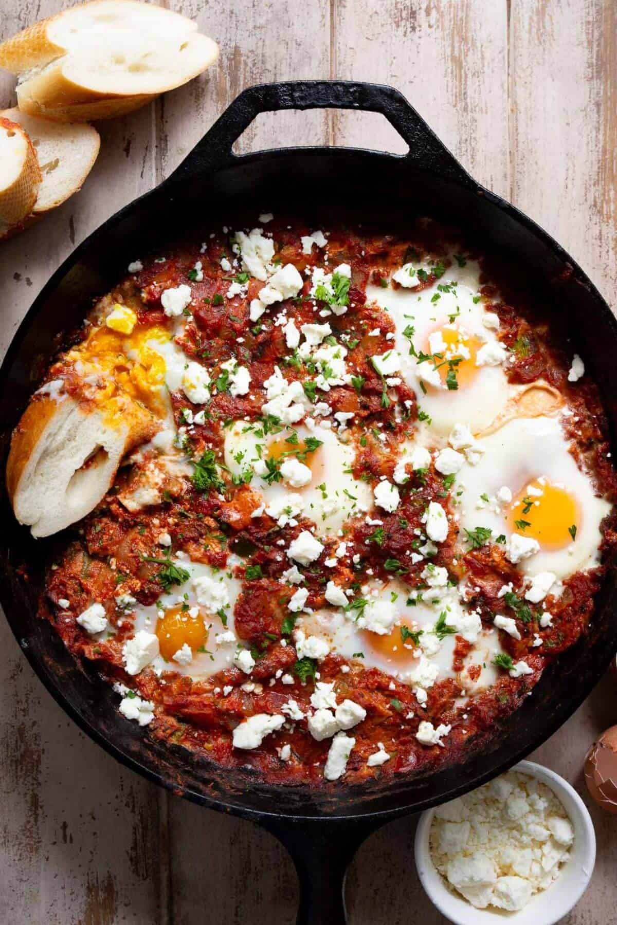 Finished Mediterranean shakshuka in a cast iron skillet topped with crumbled feta and fresh herbs