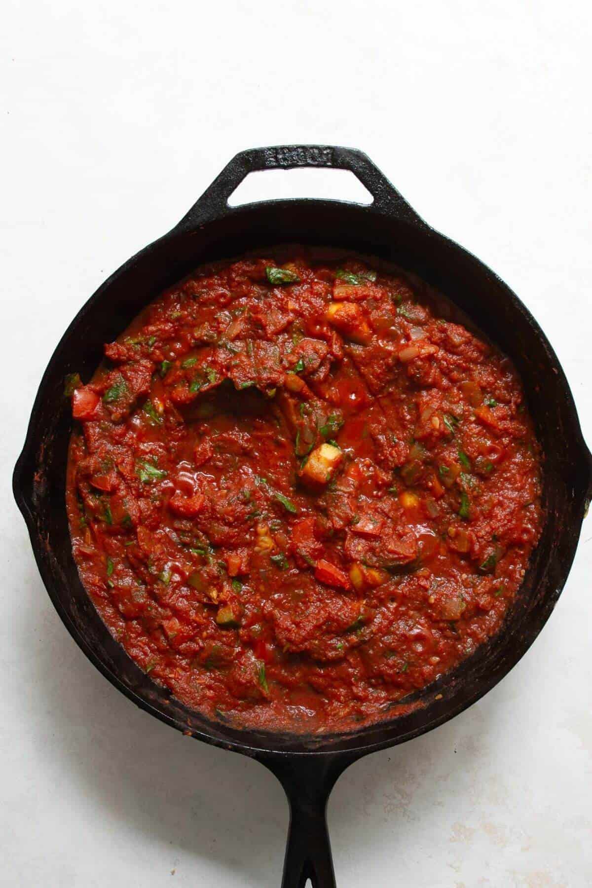 Adding canned crushed tomatoes to a cast iron pan with peppers and onions