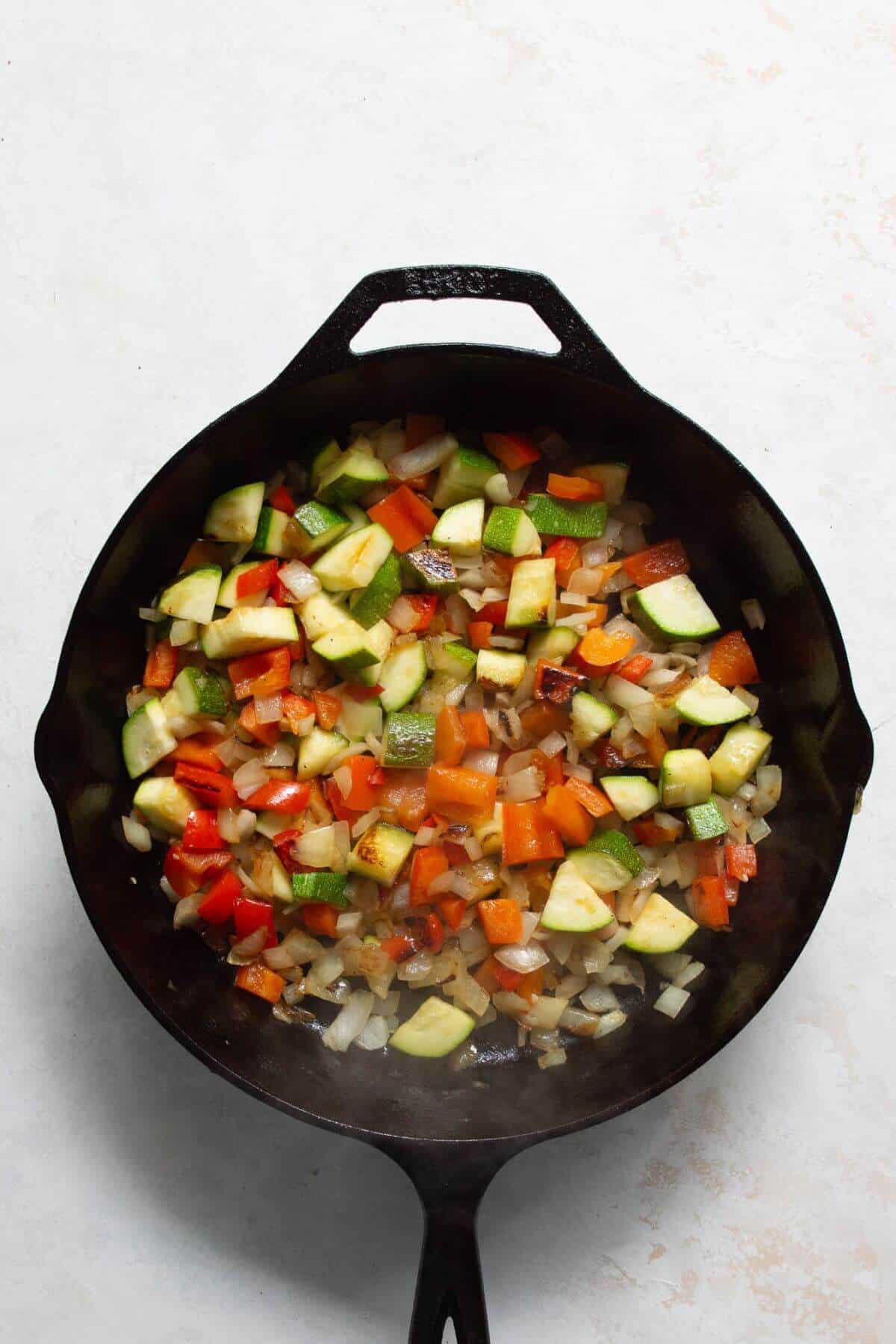 Sautéing onion, bell pepper, and zucchini in a cast iron skillet for shakshuka