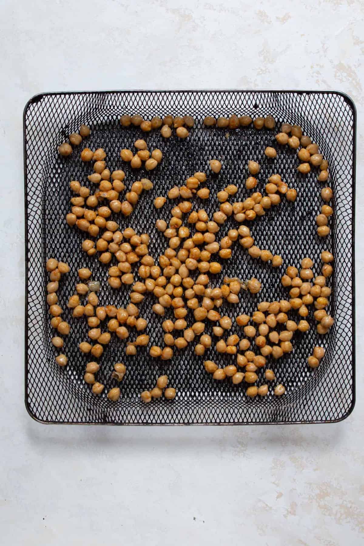 Seasoned chickpeas spread in a single layer in the air fryer basket before cooking
